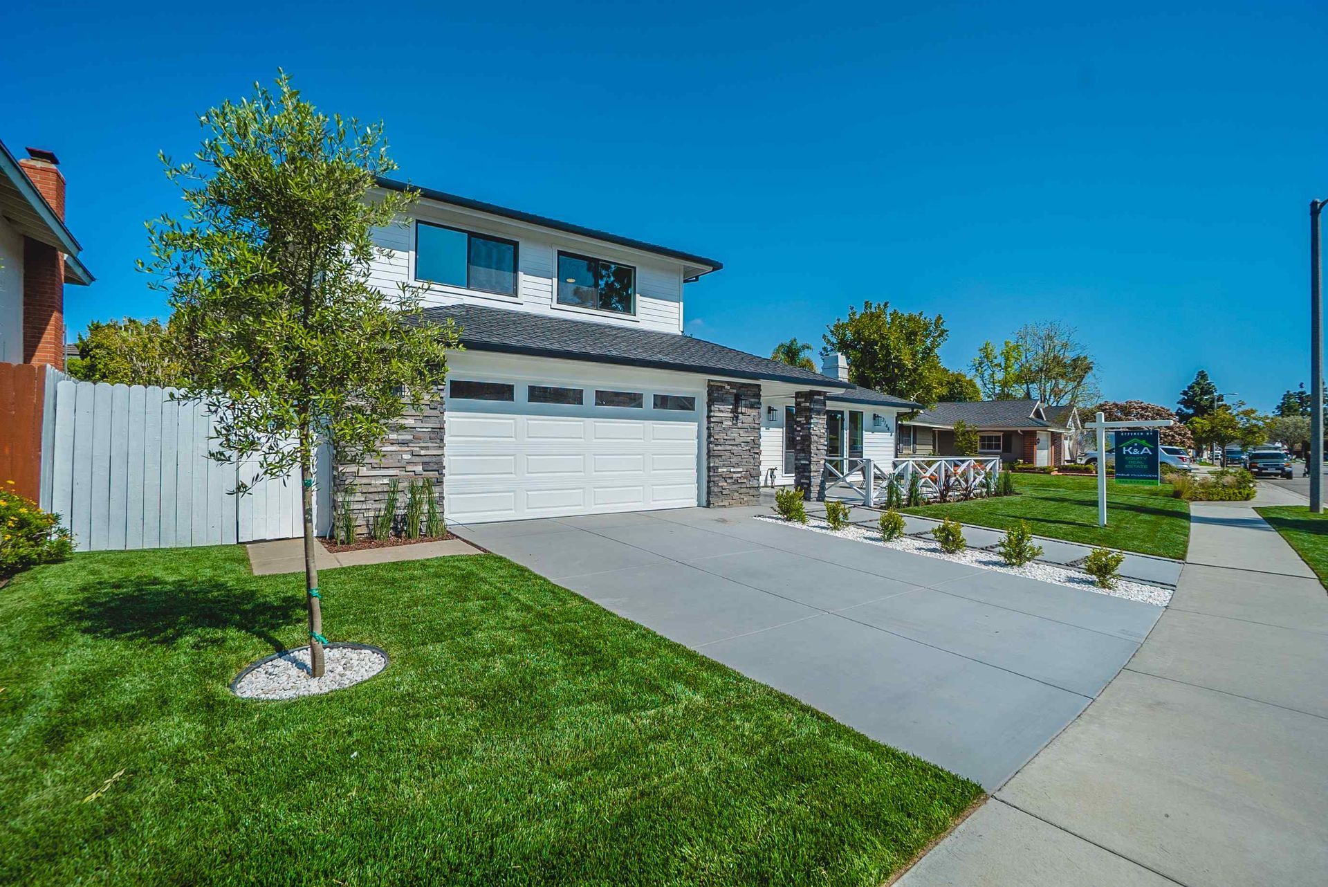 Two-story white house with a garage, lawn, and driveway under a clear blue sky.