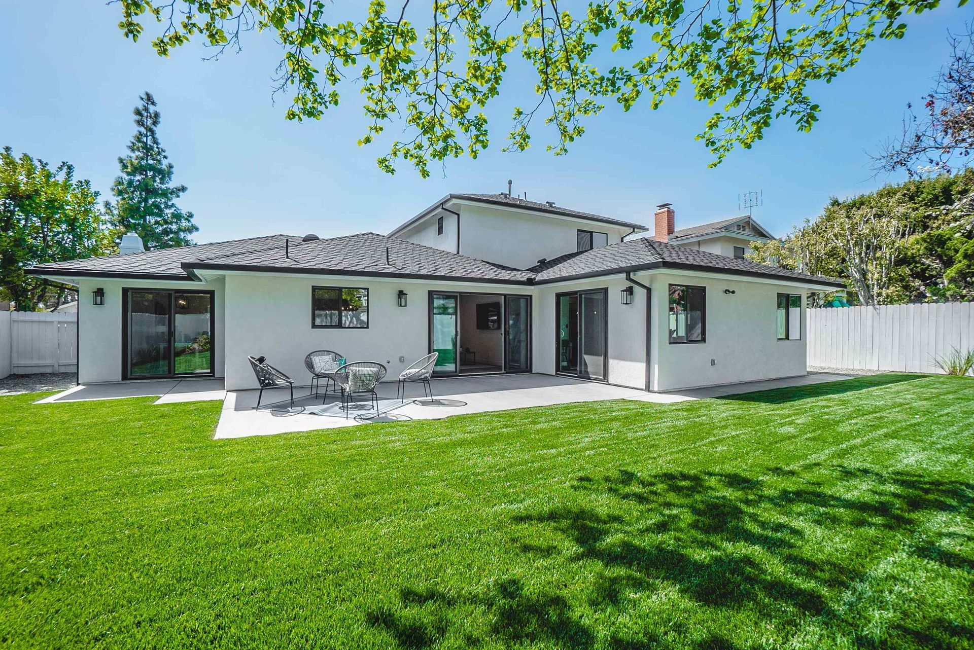 White house with black trim, patio, and green lawn under a sunny sky.