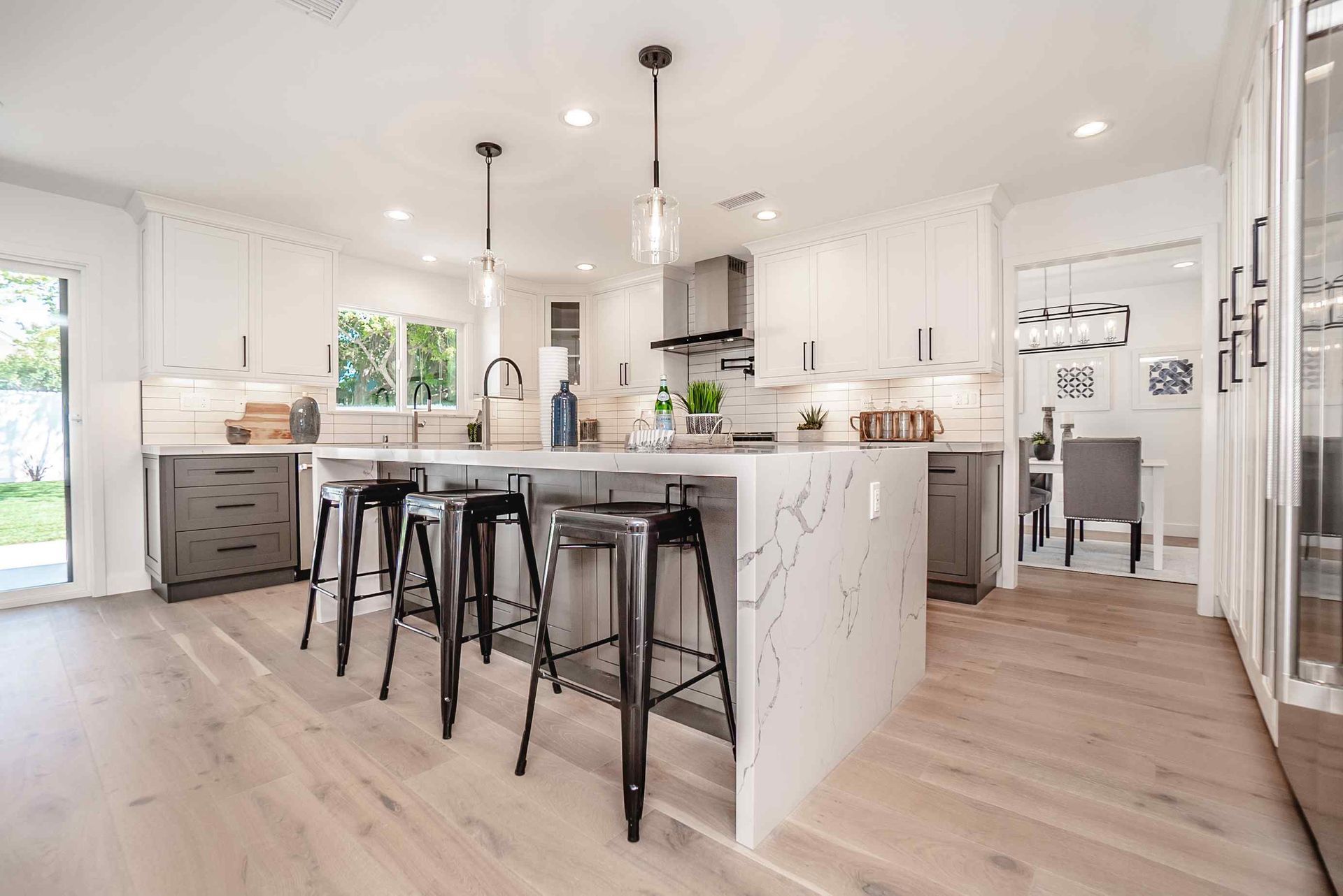 Modern kitchen with white cabinets, large island, black bar stools, and light wood flooring.