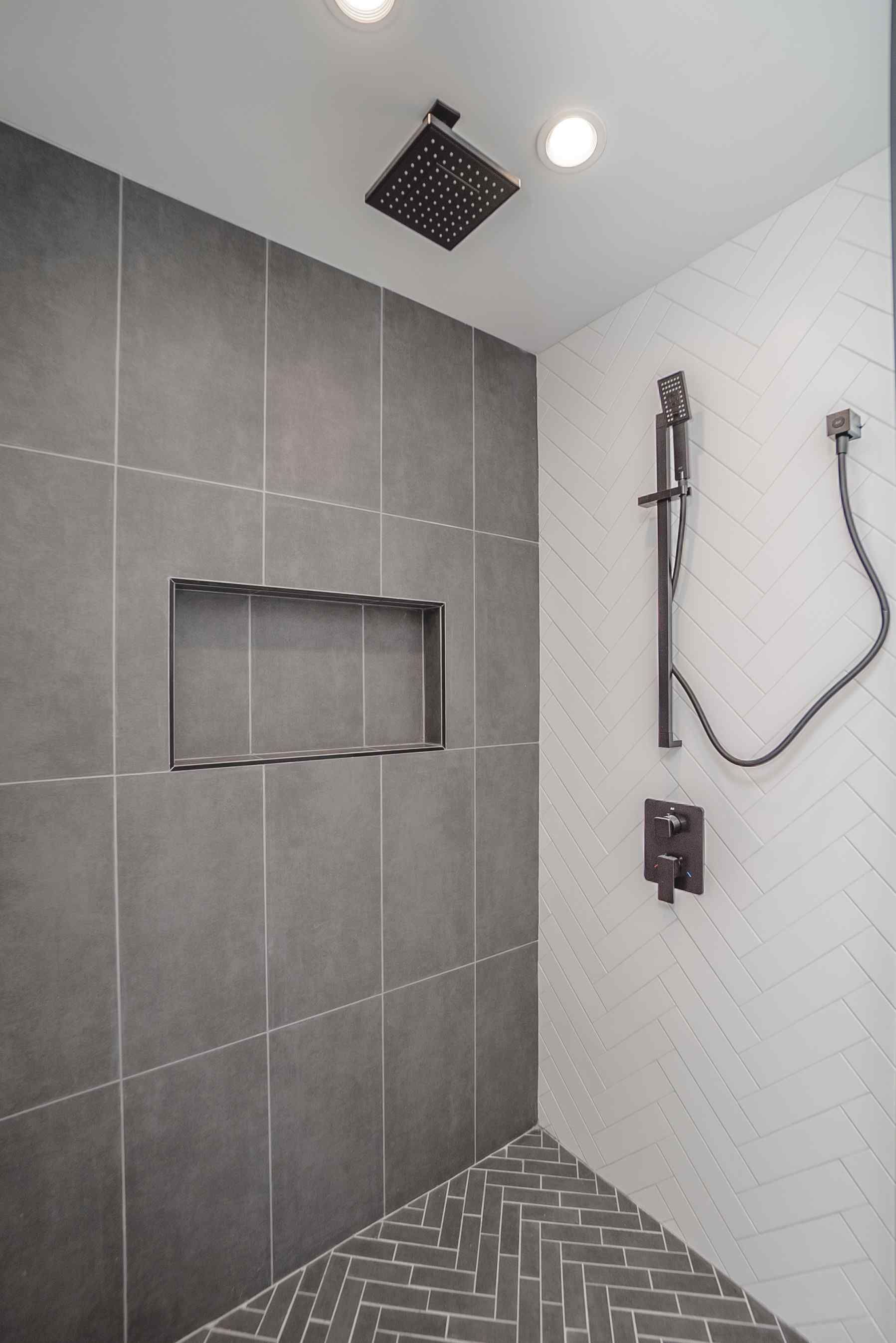 Modern shower with gray tiled walls and a herringbone floor, black fixtures.