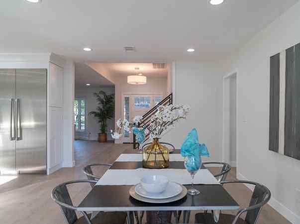 Dining room with table set for a meal, leading to an entryway and kitchen. Modern design with neutral colors.