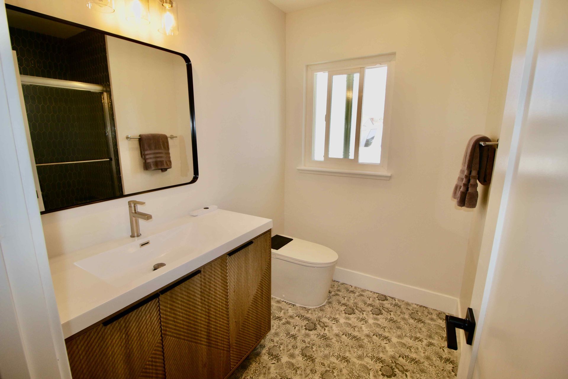 Modern bathroom with wood vanity, large mirror, white toilet, and textured tile floor
