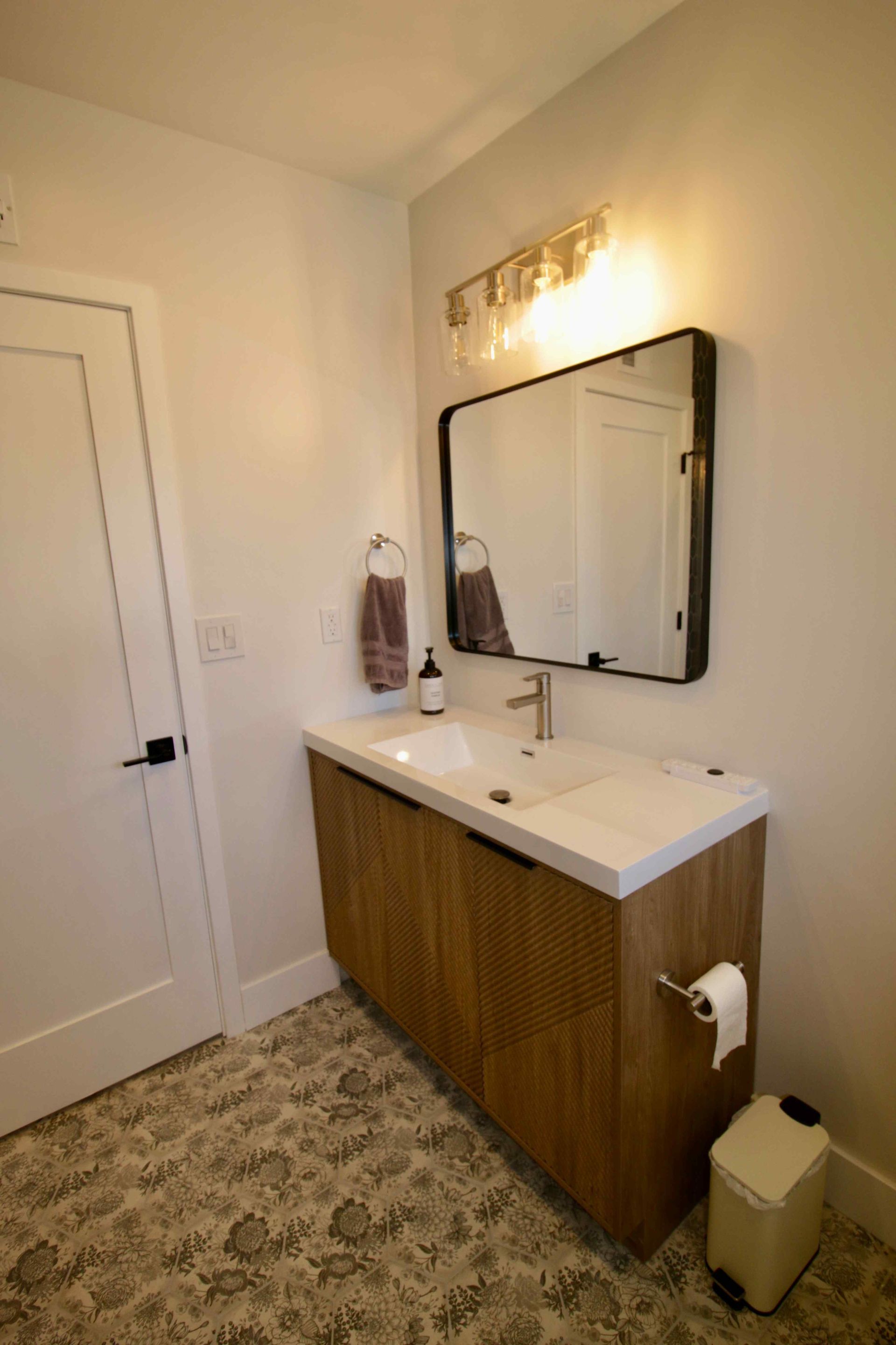 Small bathroom vanity with mirror, sink, towel ring, and wall light beside a white door.