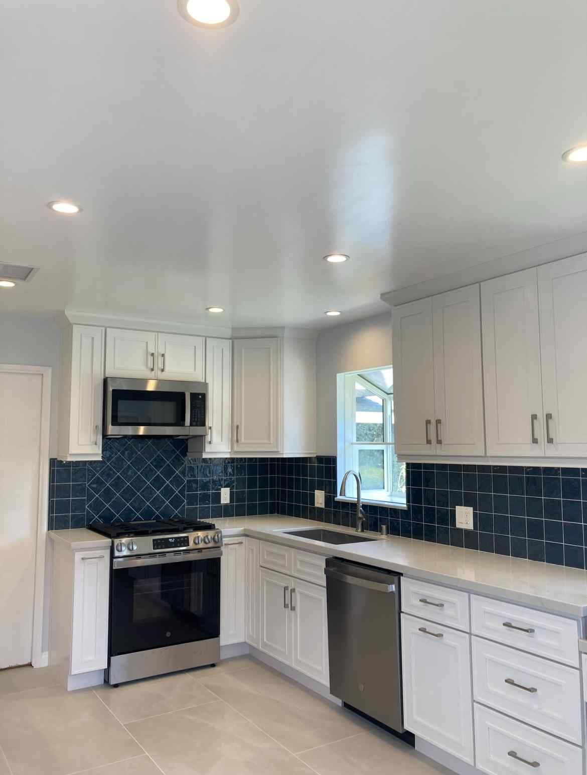 Bright kitchen with white cabinets, stainless steel appliances, and dark blue tile backsplash.