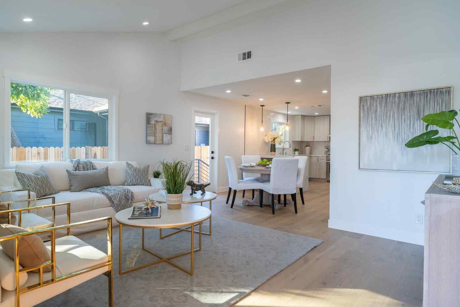 Bright, airy living room with white sofas, gold tables, and a dining area beyond.