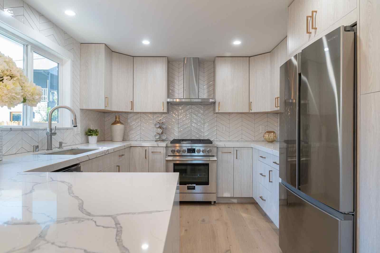 Bright modern kitchen with white cabinets, marble countertops, stainless steel appliances, and a large island.