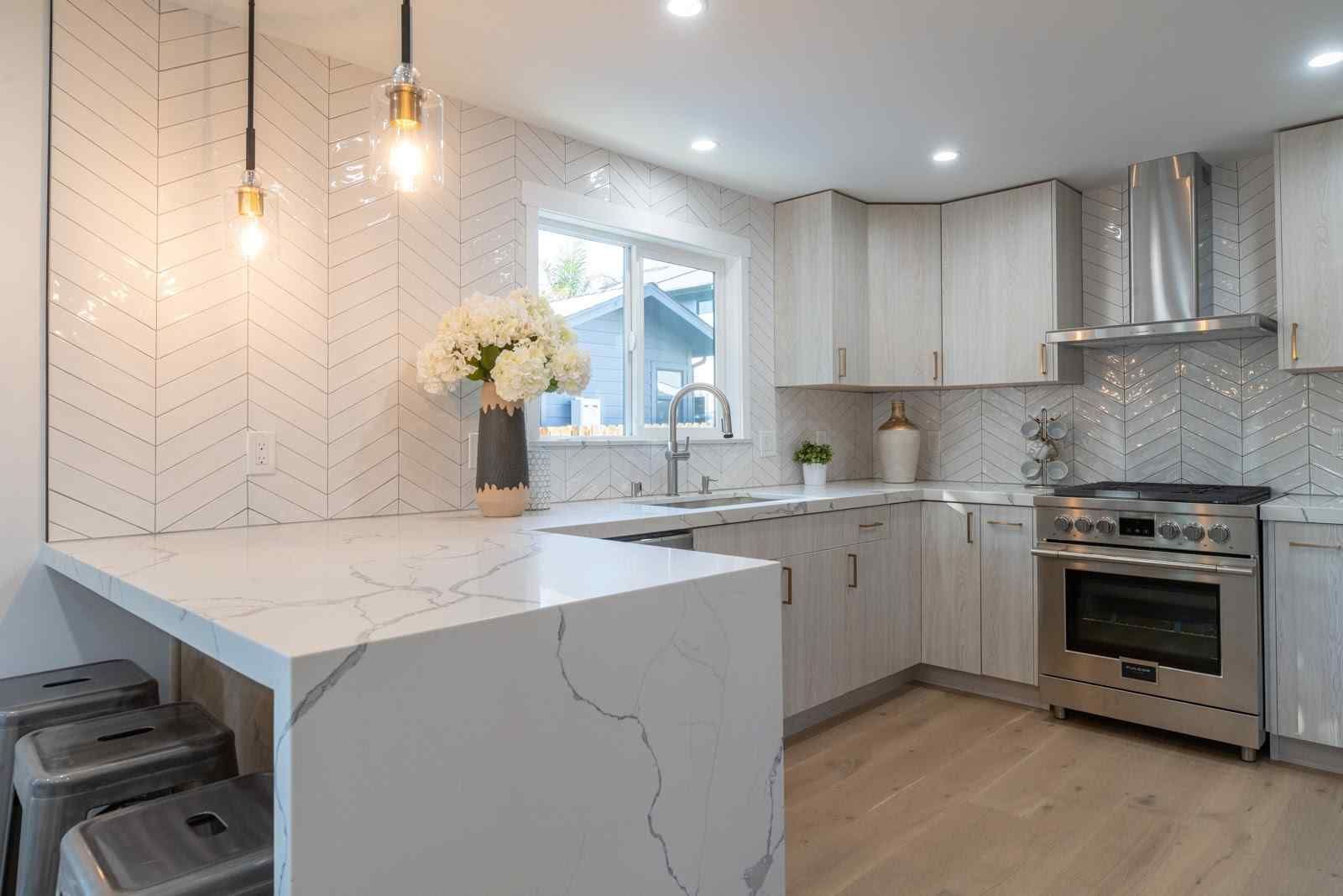 Modern white kitchen with marble island, pendant lights, stainless steel stove, and tiled backsplash