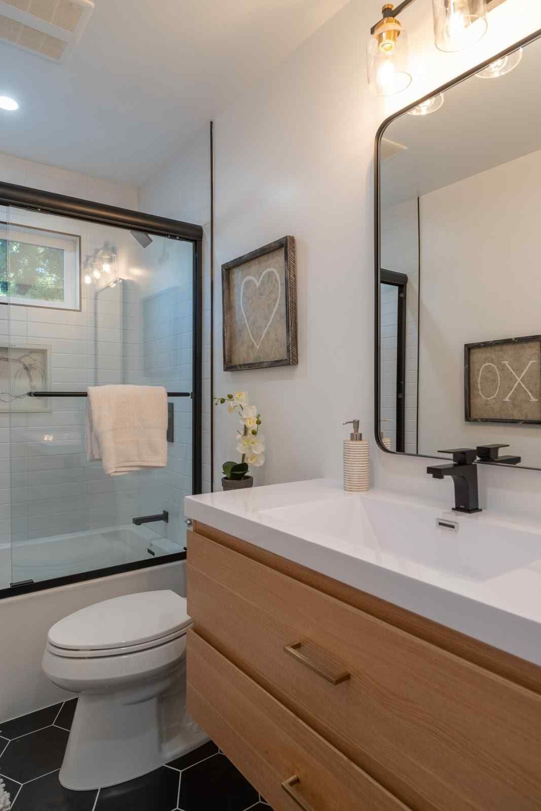 Modern bathroom with glass shower, toilet, wood vanity, black-framed mirror, and white countertop
