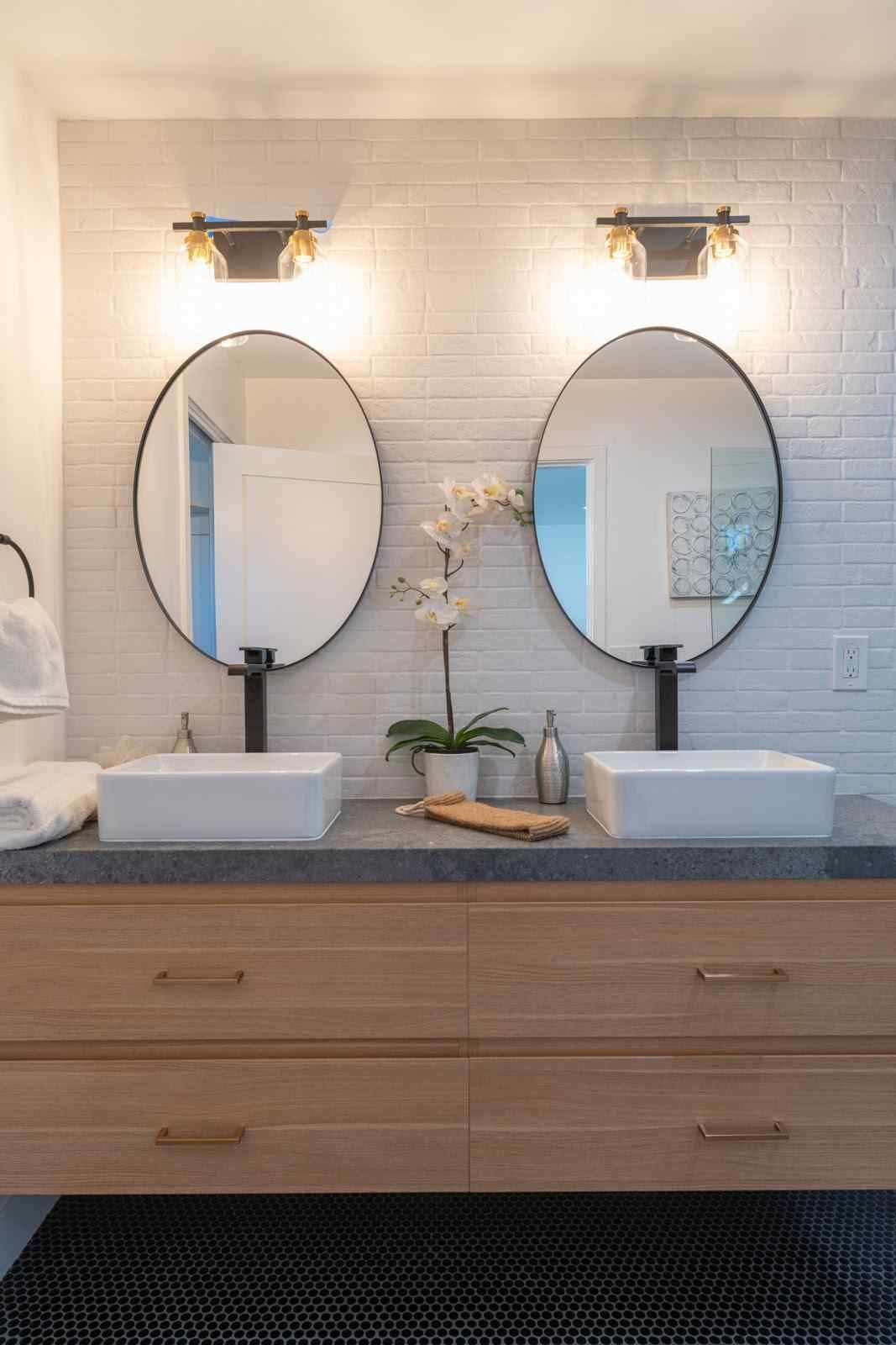 Modern double vanity with oval mirrors, wall sconces, and wood cabinets in a bright bathroom