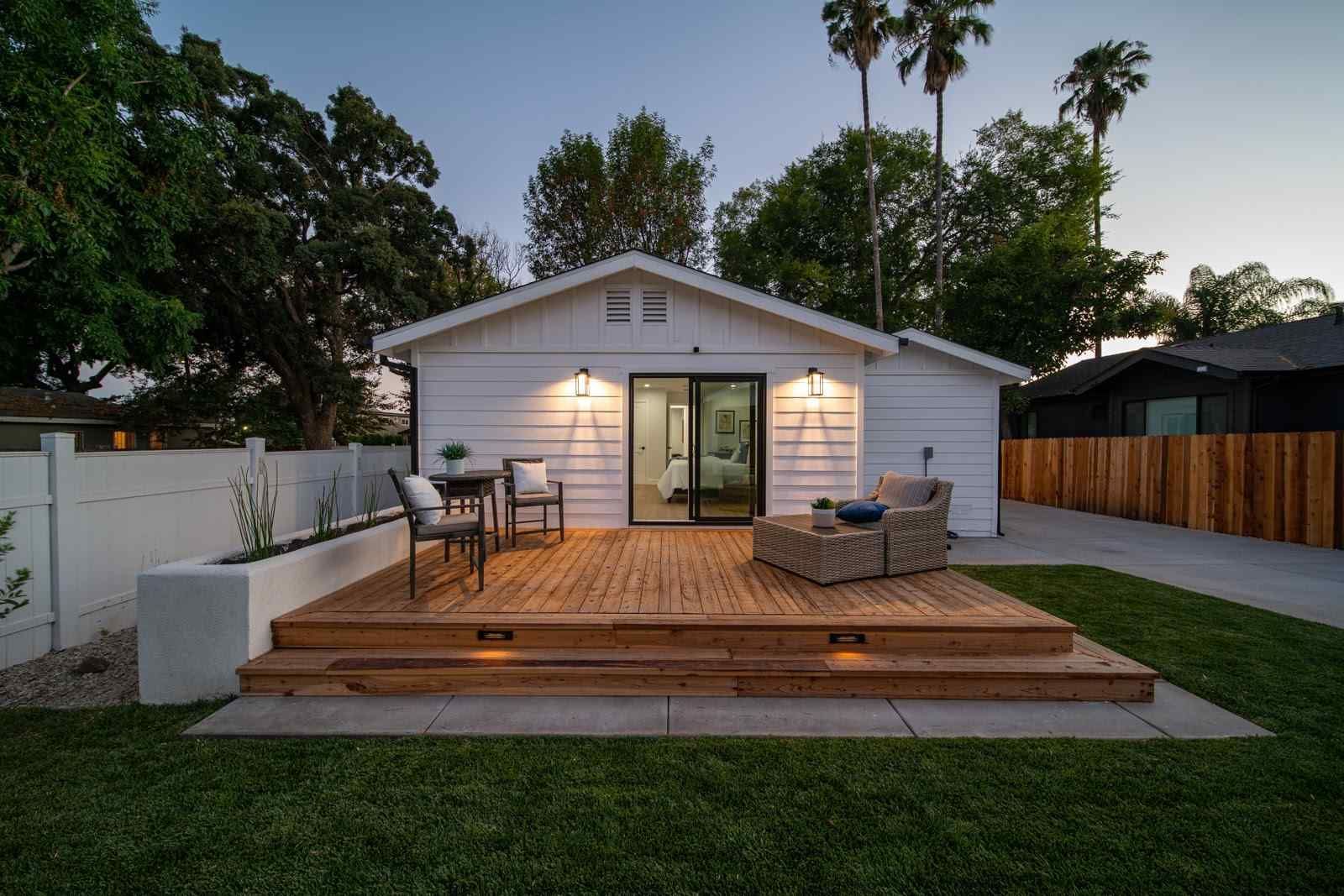 Backyard deck with outdoor seating and a lit white house at dusk