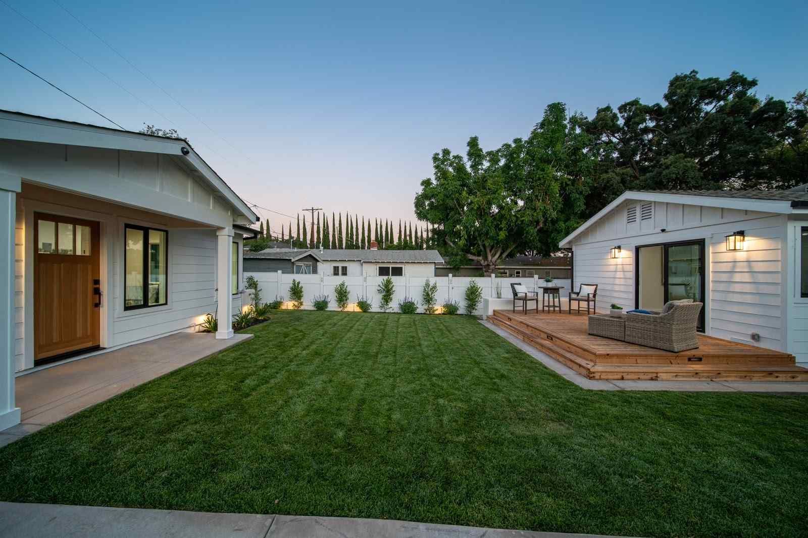 Backyard with green lawn, white patio buildings, and a small deck at dusk