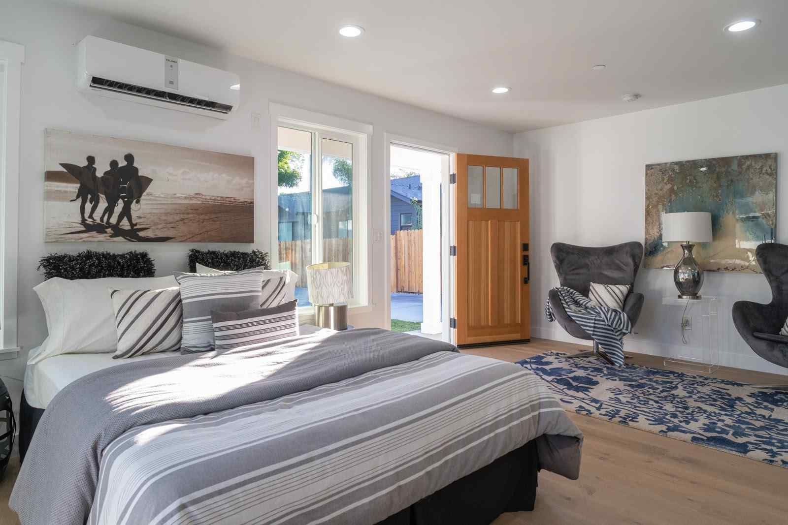 Bright bedroom with striped bed, wall art, open door, and a chair by the window