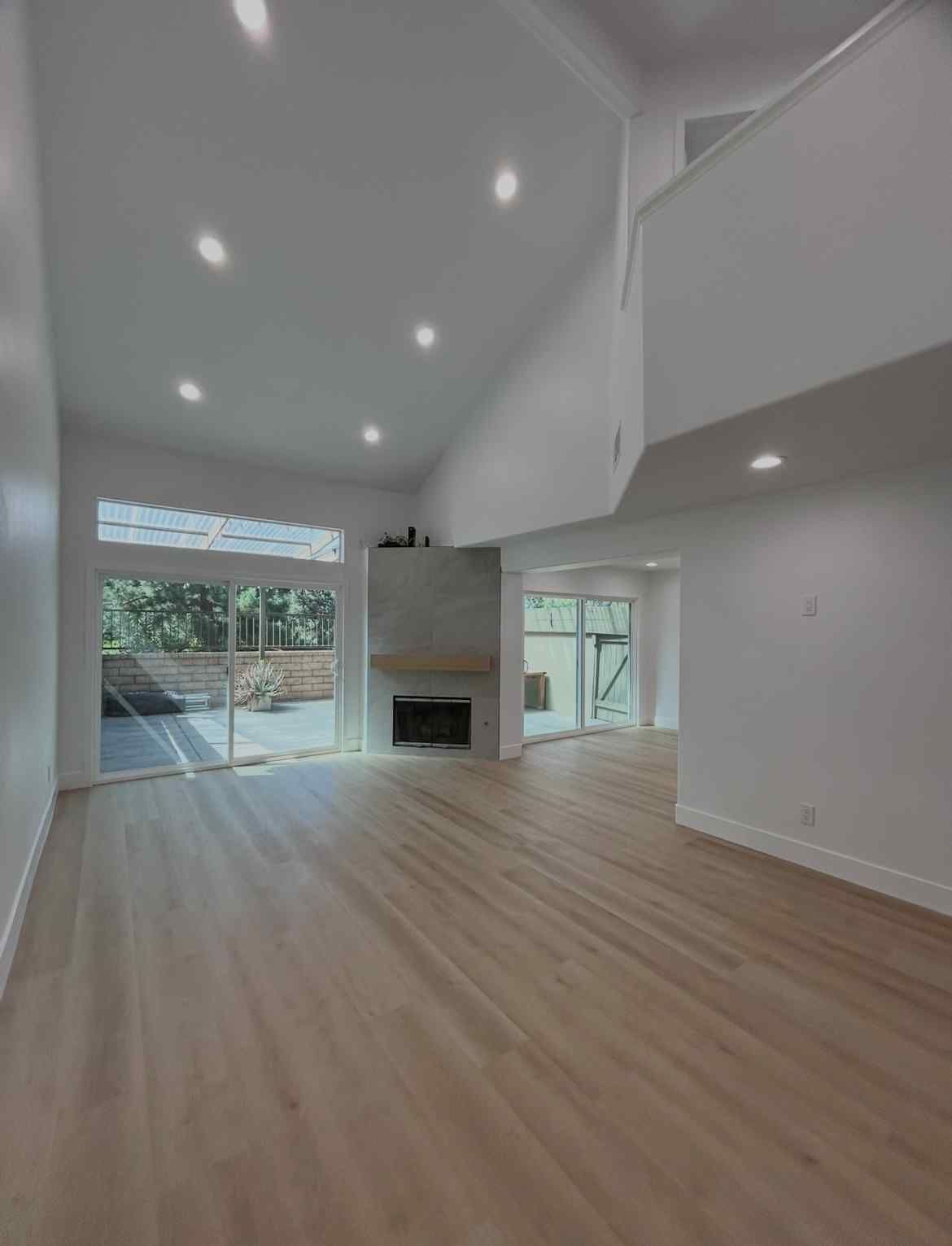 Bright empty living room with vaulted ceiling, wood floors, fireplace, and large sliding glass doors