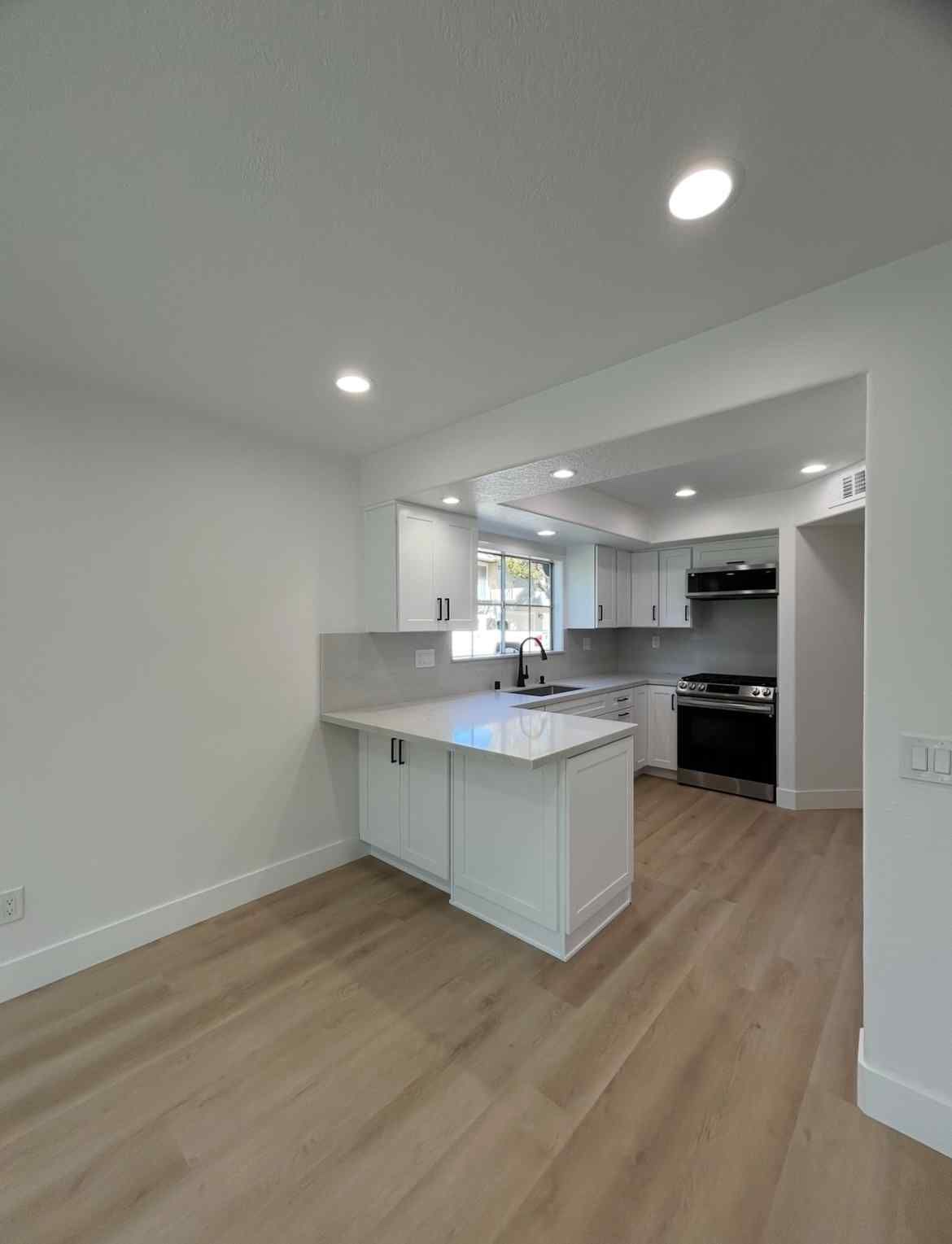Modern white kitchen with island, light wood floors, recessed lights, and stainless steel appliances
