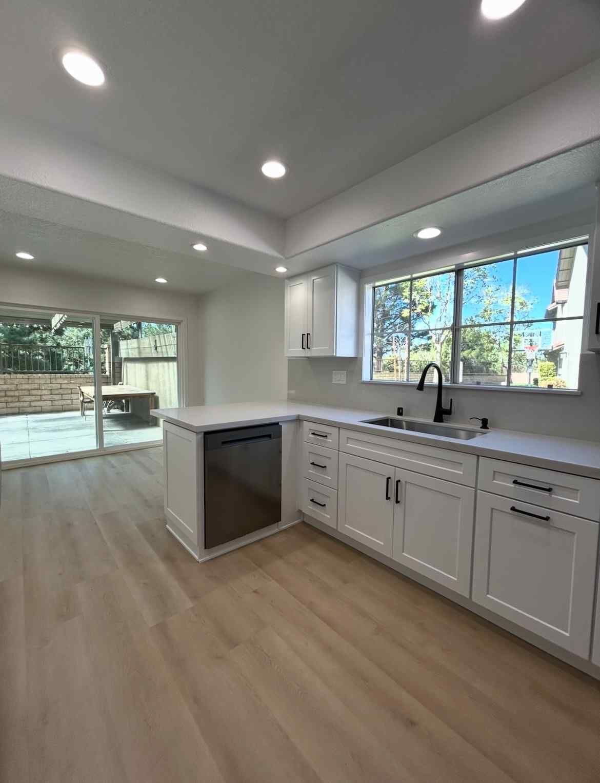 Bright modern kitchen with white cabinets, light wood floors, and large windows overlooking a patio