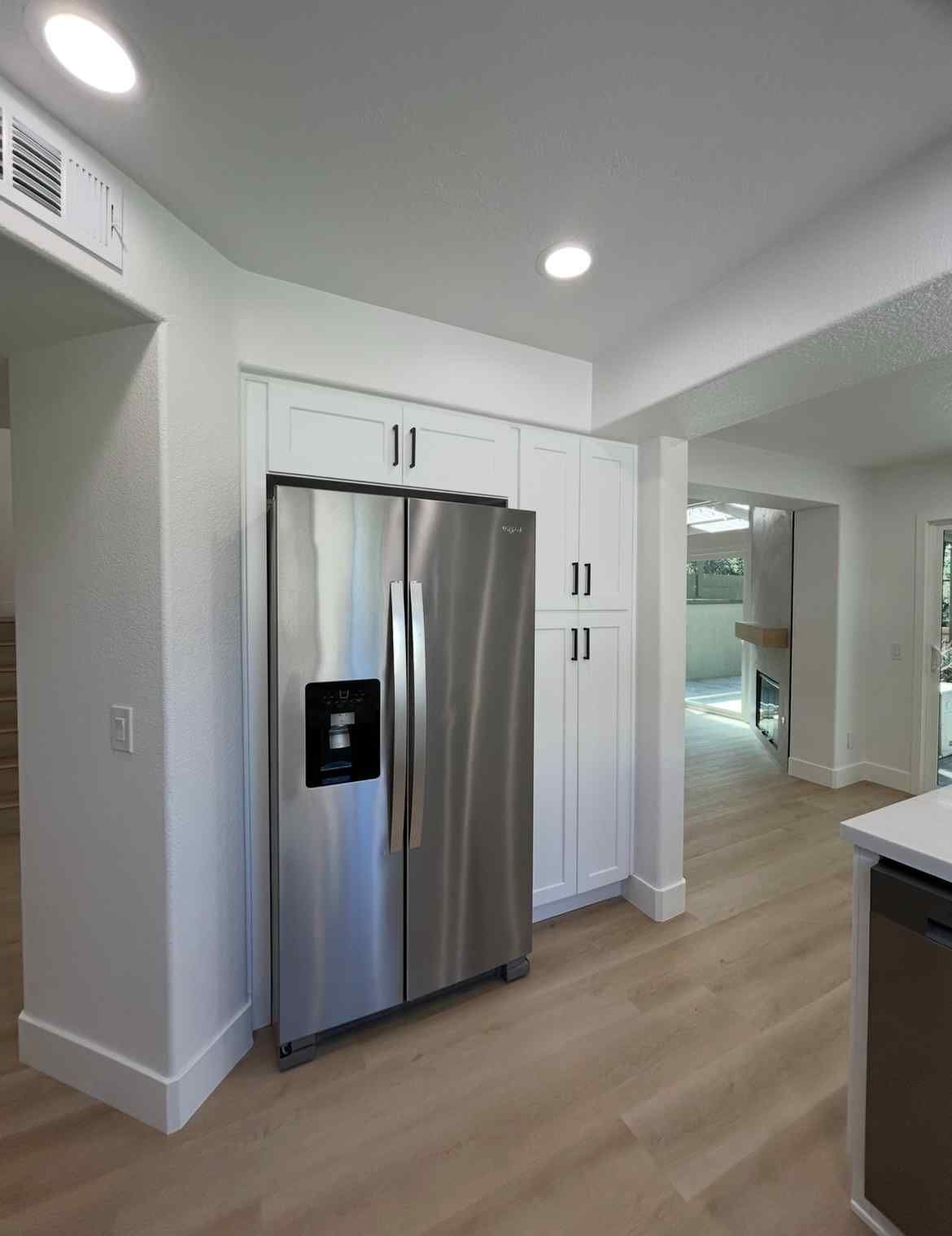 Modern kitchen with stainless steel refrigerator, white cabinets, and light wood flooring.