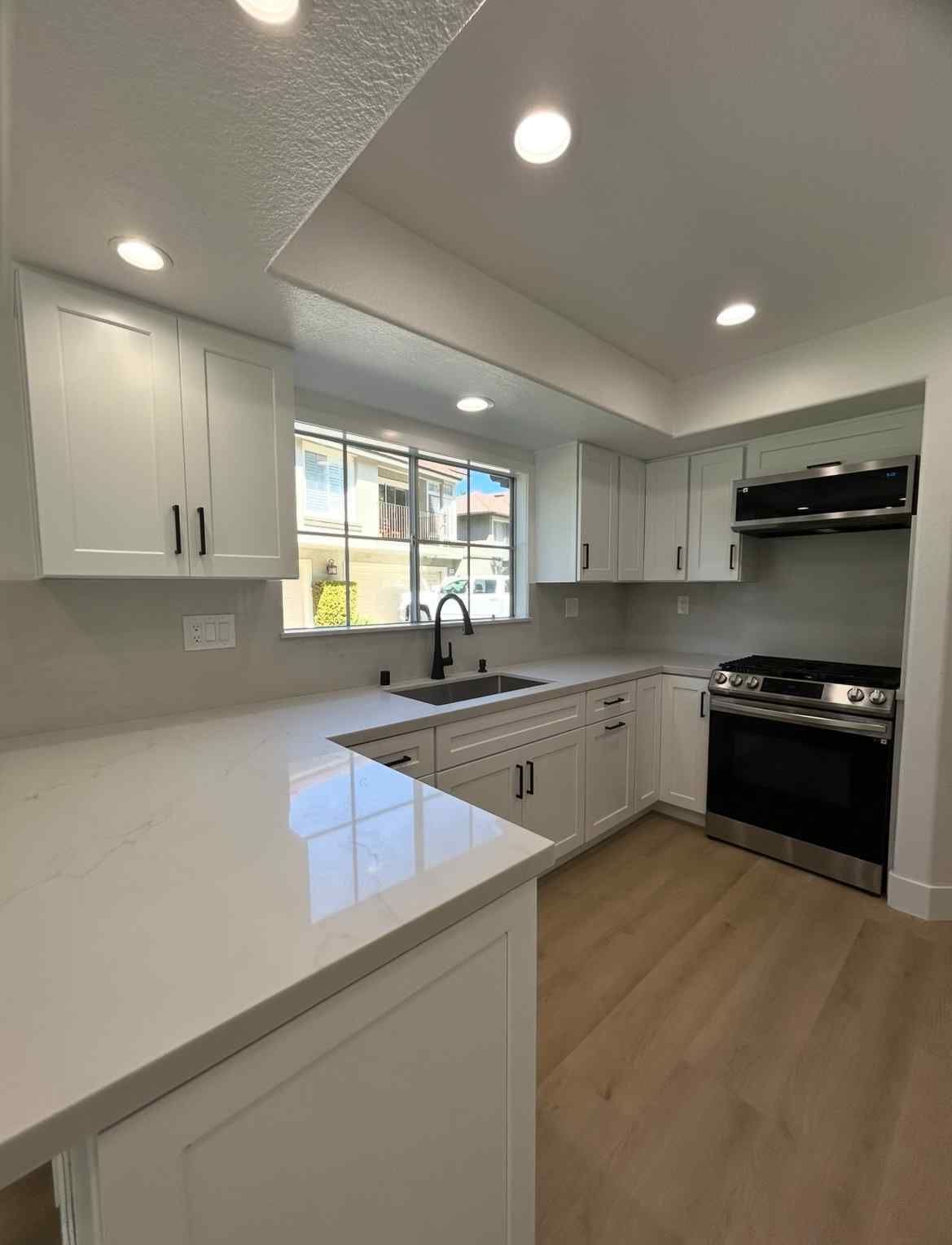 Bright modern white kitchen with island, stainless appliances, and wood floors