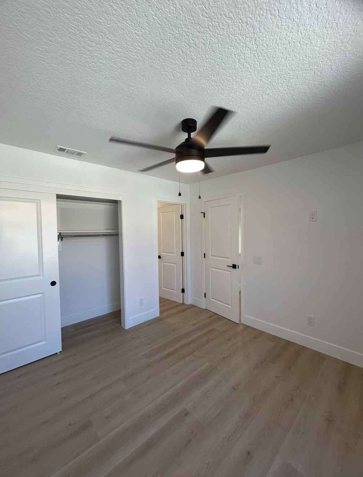 Empty white bedroom with wood floor, ceiling fan, two closets, and closed door