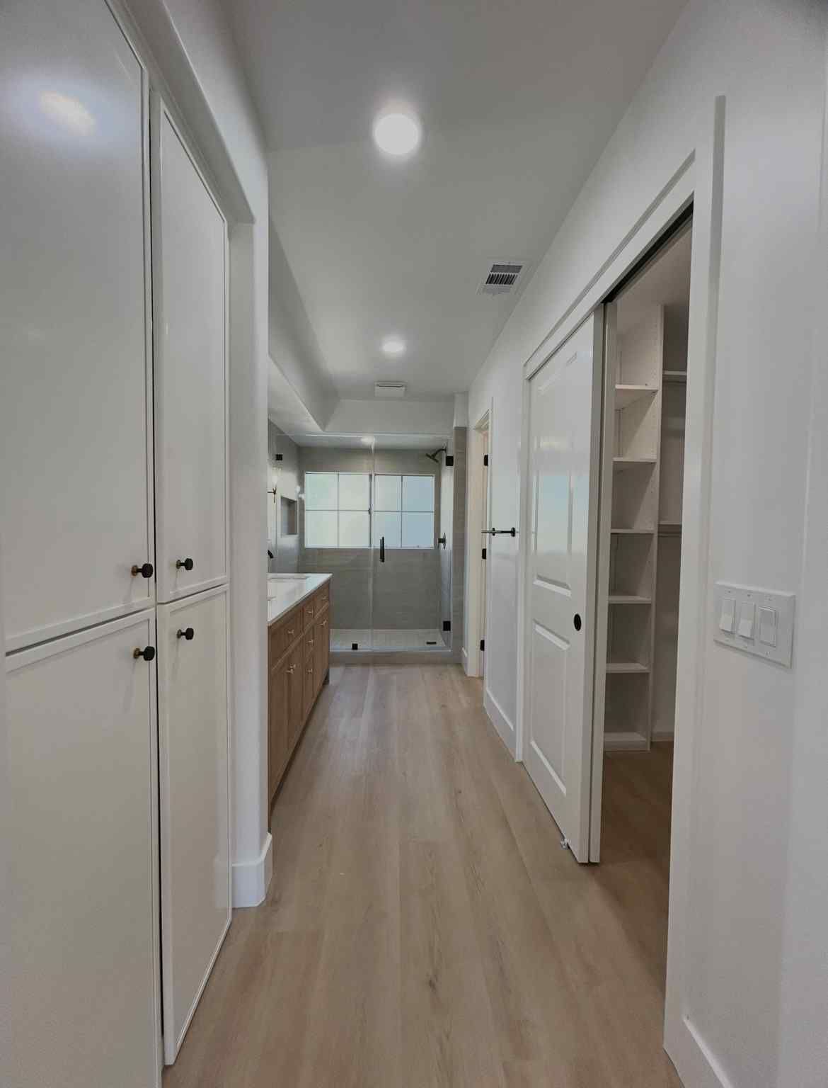 Bright modern hallway with white walls, wood floors, built-in cabinets, and open doorways.