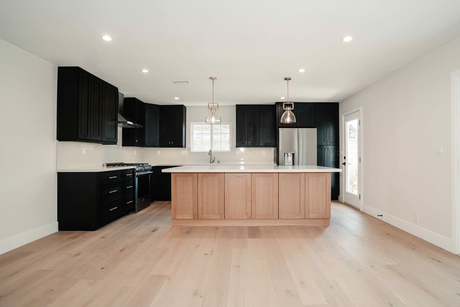 Modern open kitchen with black cabinets, wood island, light floors, and recessed ceiling lights