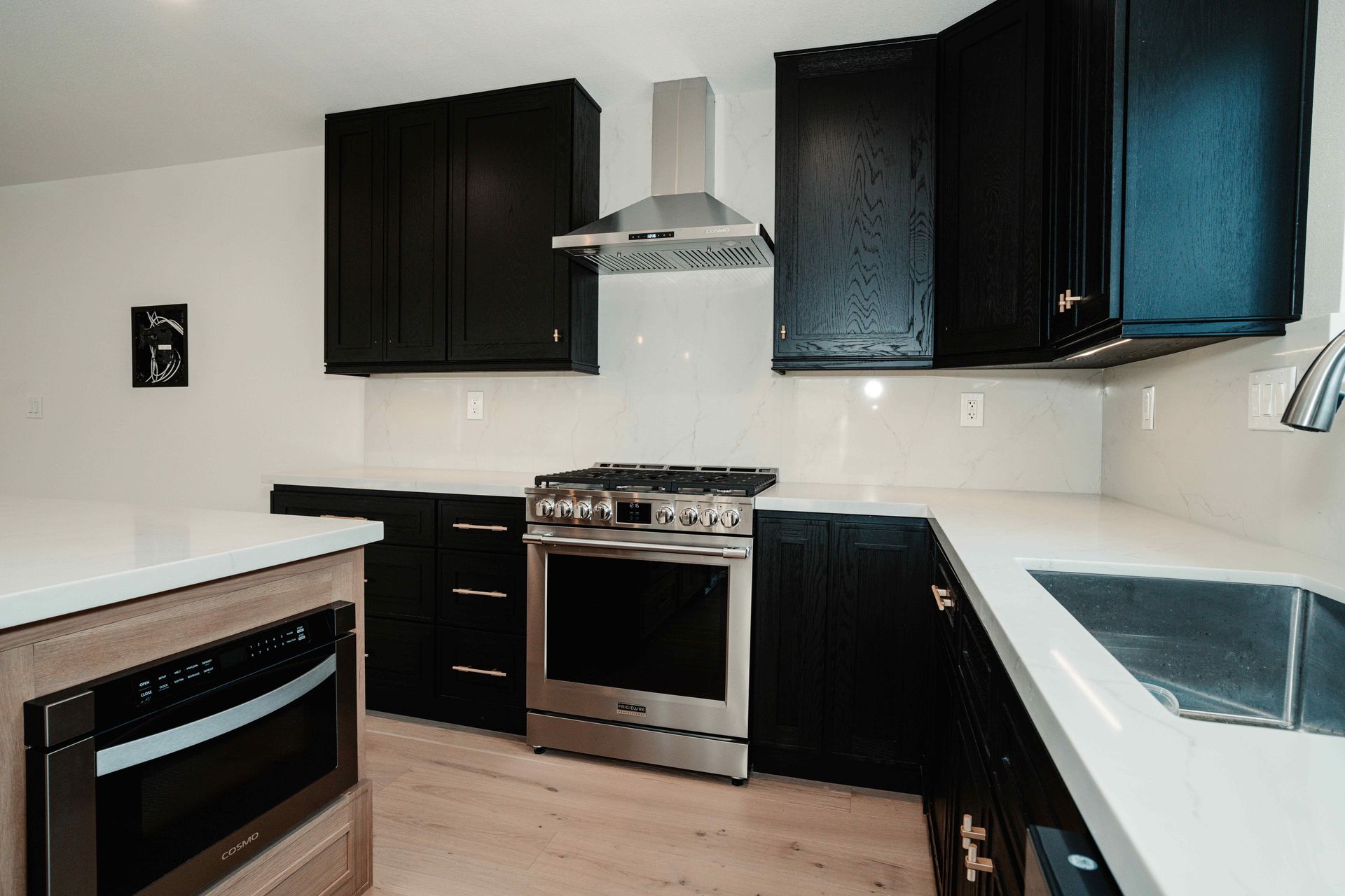 Modern kitchen with black cabinets, stainless steel appliances, and white countertops