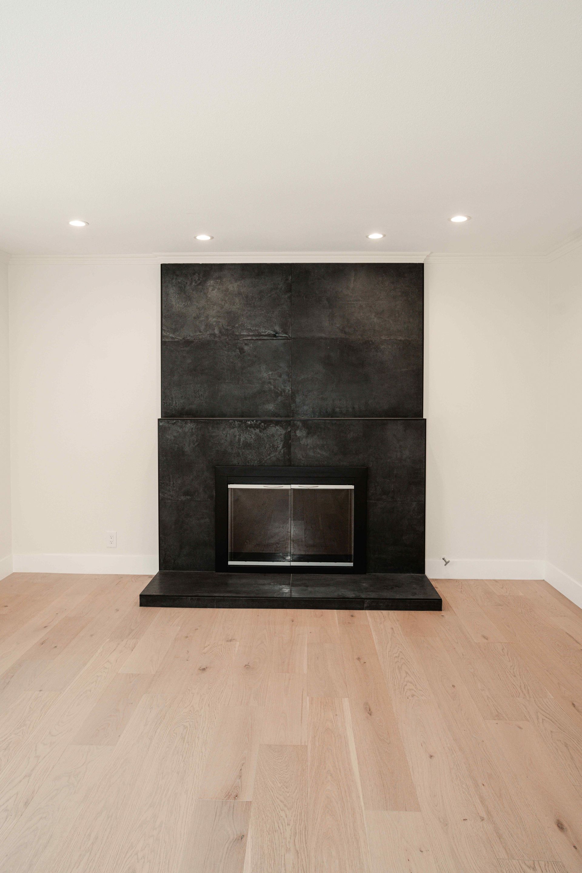 Minimal living room with a black fireplace, light wood floor, and white walls