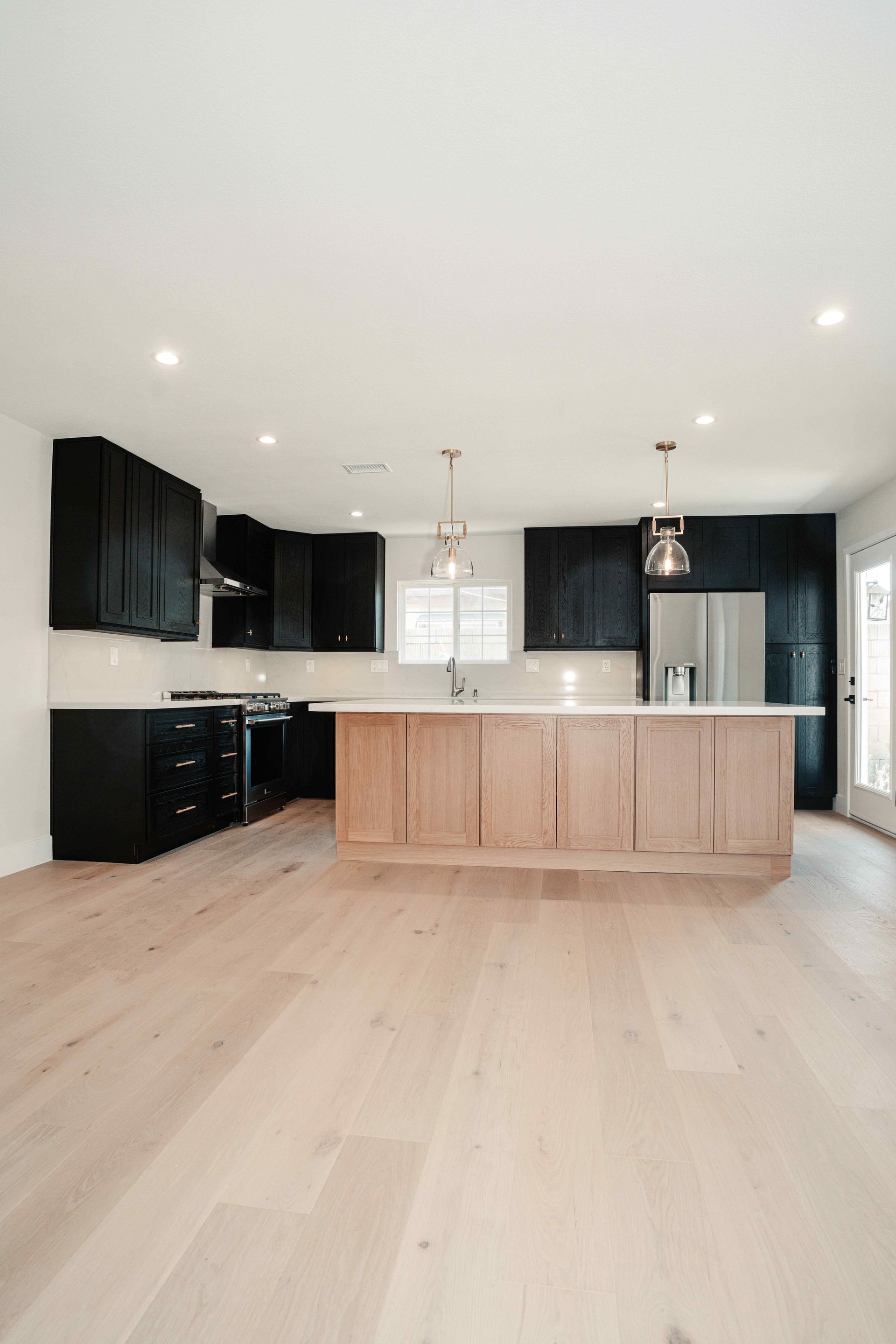 Modern kitchen with black cabinets, light wood island, and pale wood flooring in a bright open space