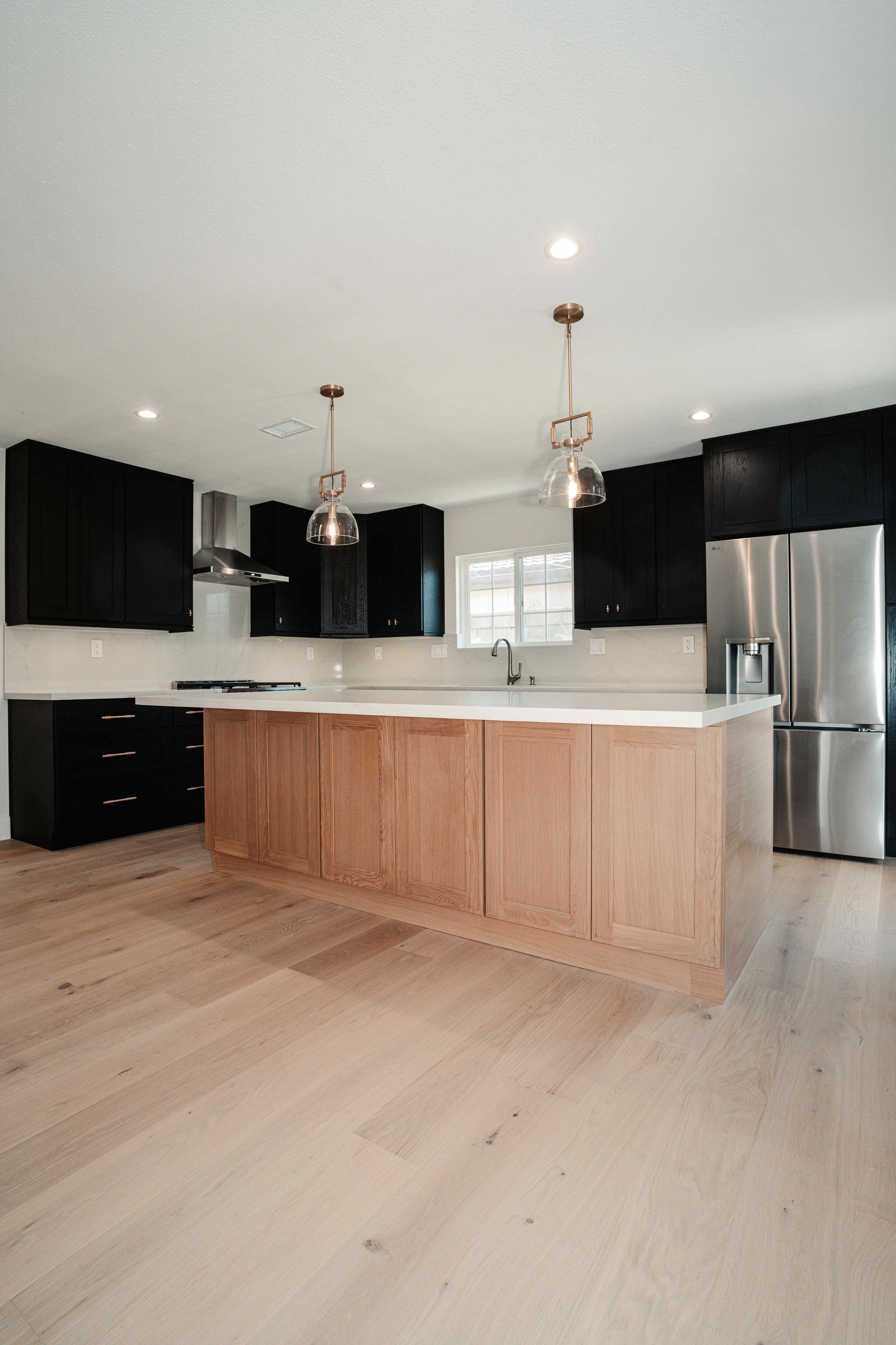 Modern kitchen with wood island, black cabinets, stainless fridge, and light wood floors