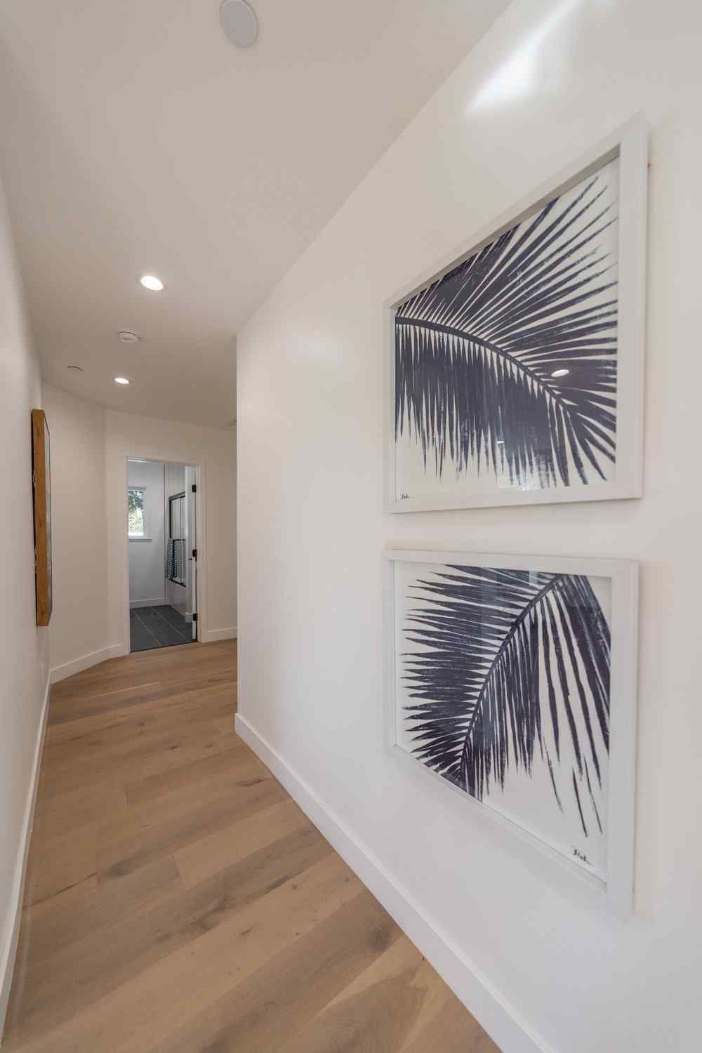 Hallway with light wood floor, white walls, and framed palm leaf prints.