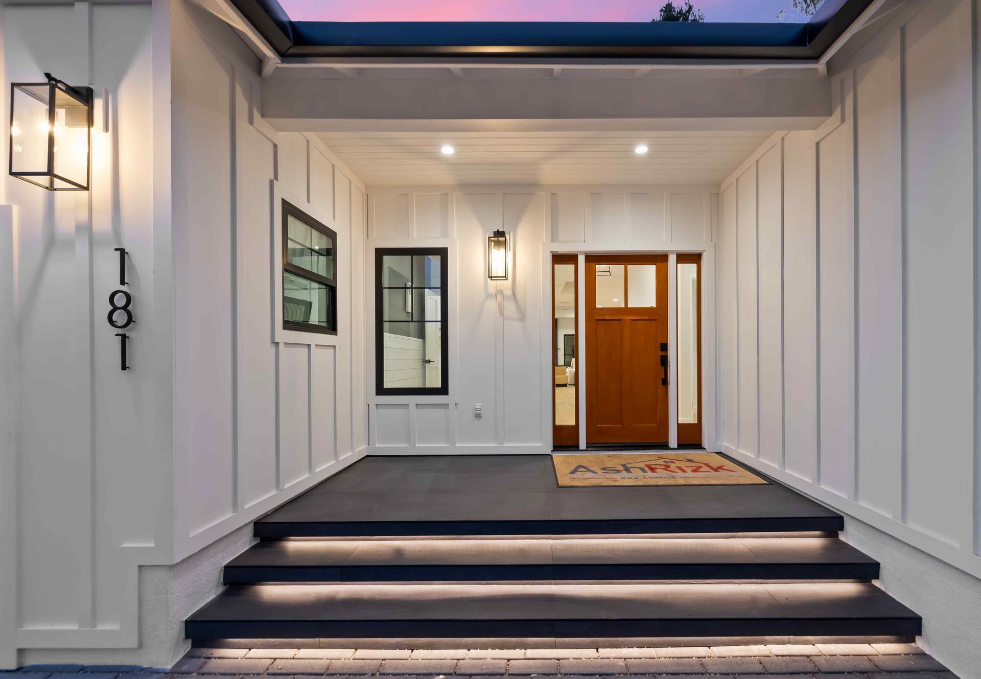 White farmhouse-style home entryway with steps and dark gray porch. Brown door with sidelight and window.