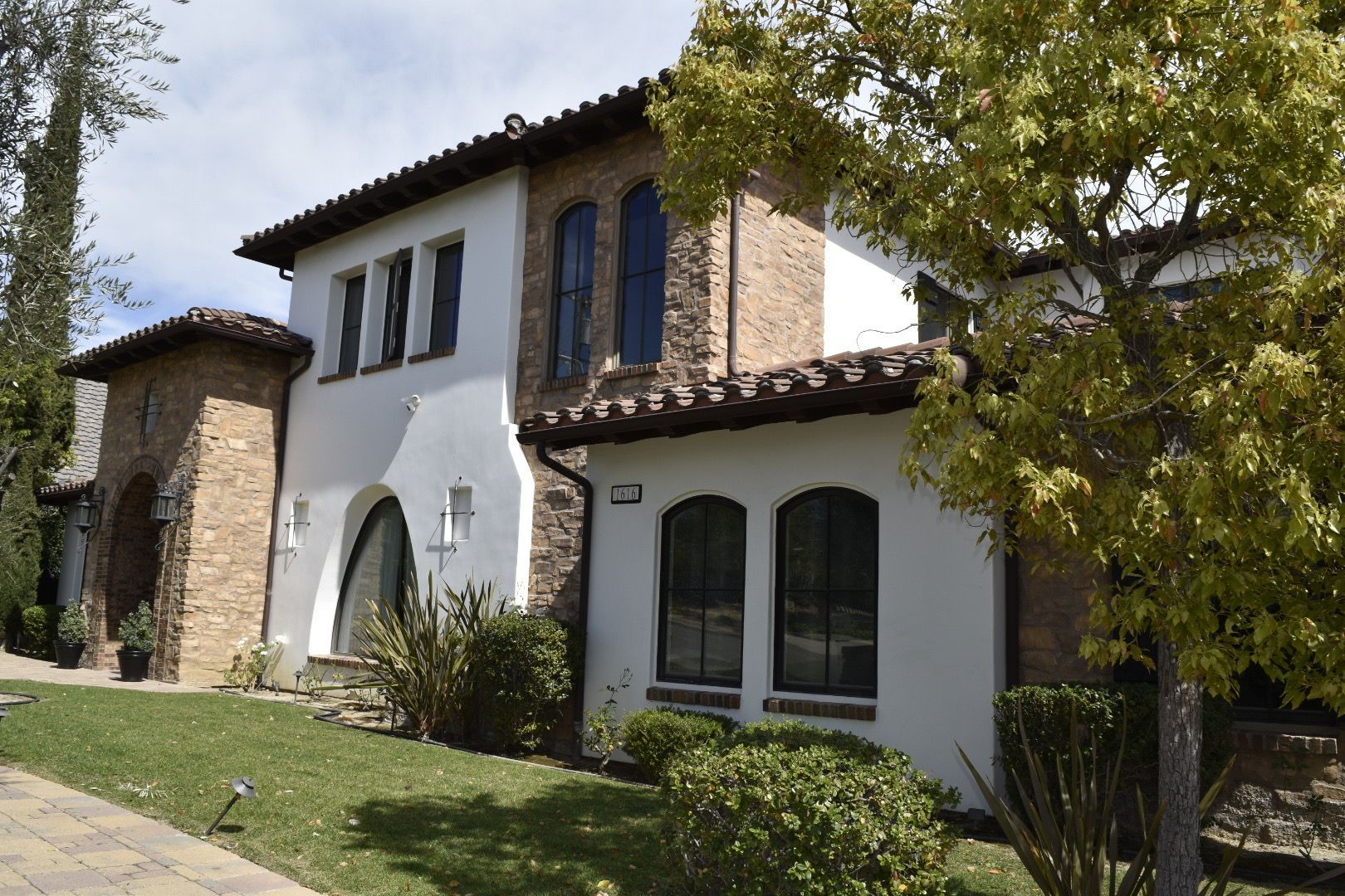Spanish-style house with white stucco walls, arched windows, and stone accents on a sunny hillside