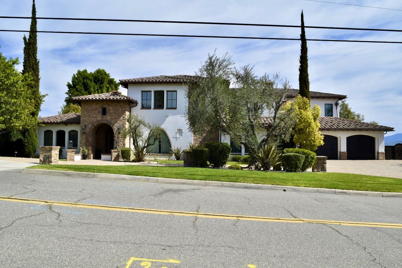 Large white stucco house with a tiled roof and arched entry, viewed from across a quiet street
