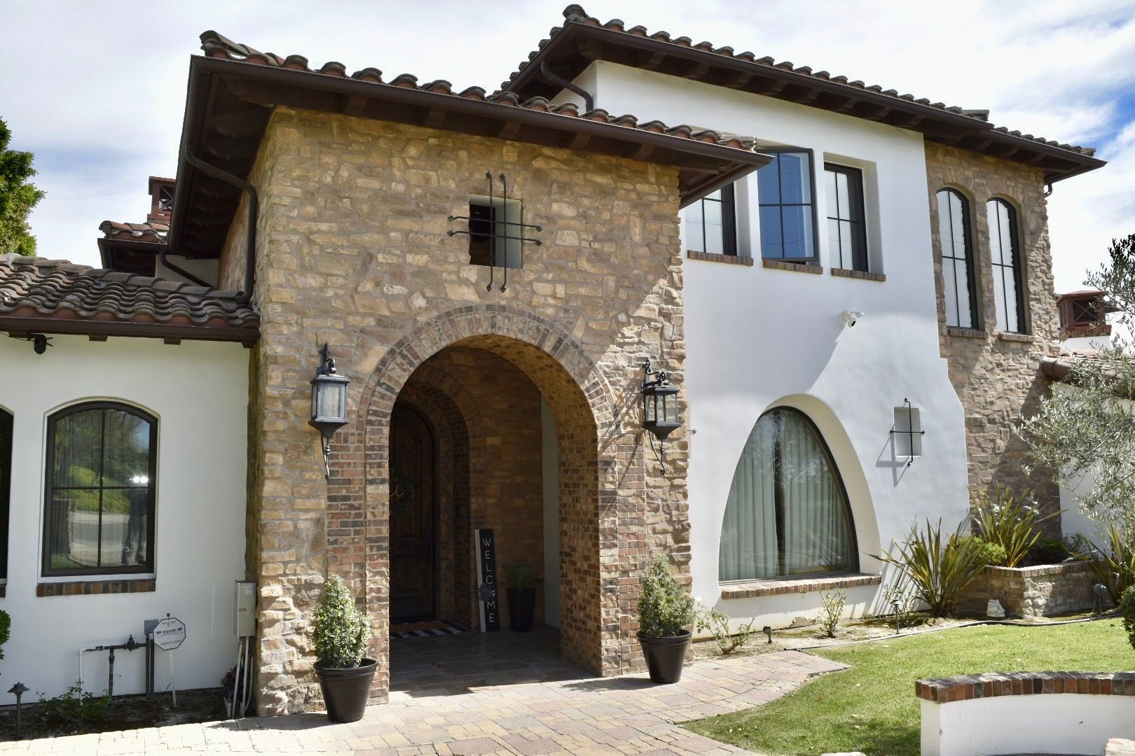 Stone and stucco house exterior with arched entryway, white walls, and tiled roof on a sunny day