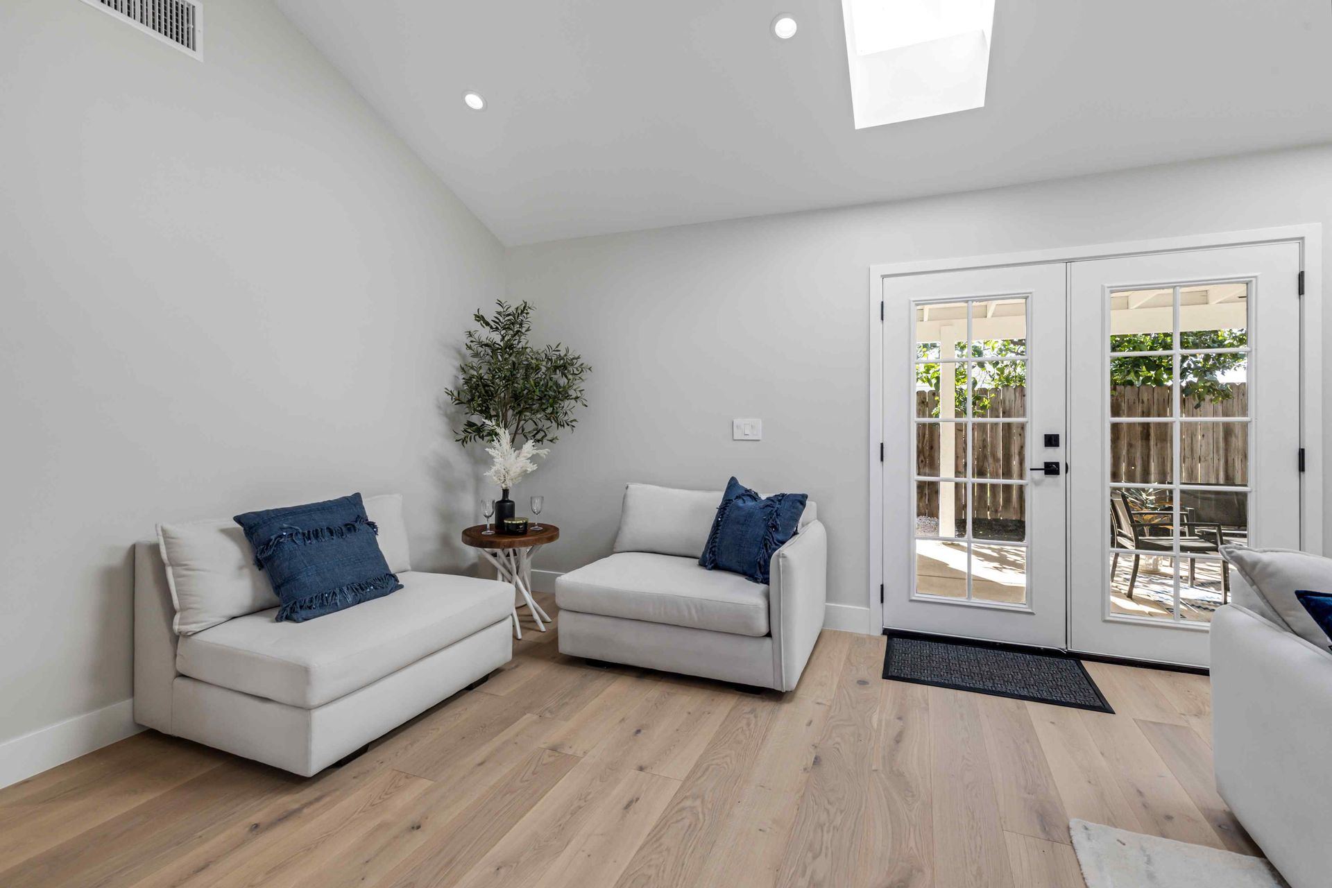 Bright living room with two white chairs, blue pillows, a small table, and French doors.