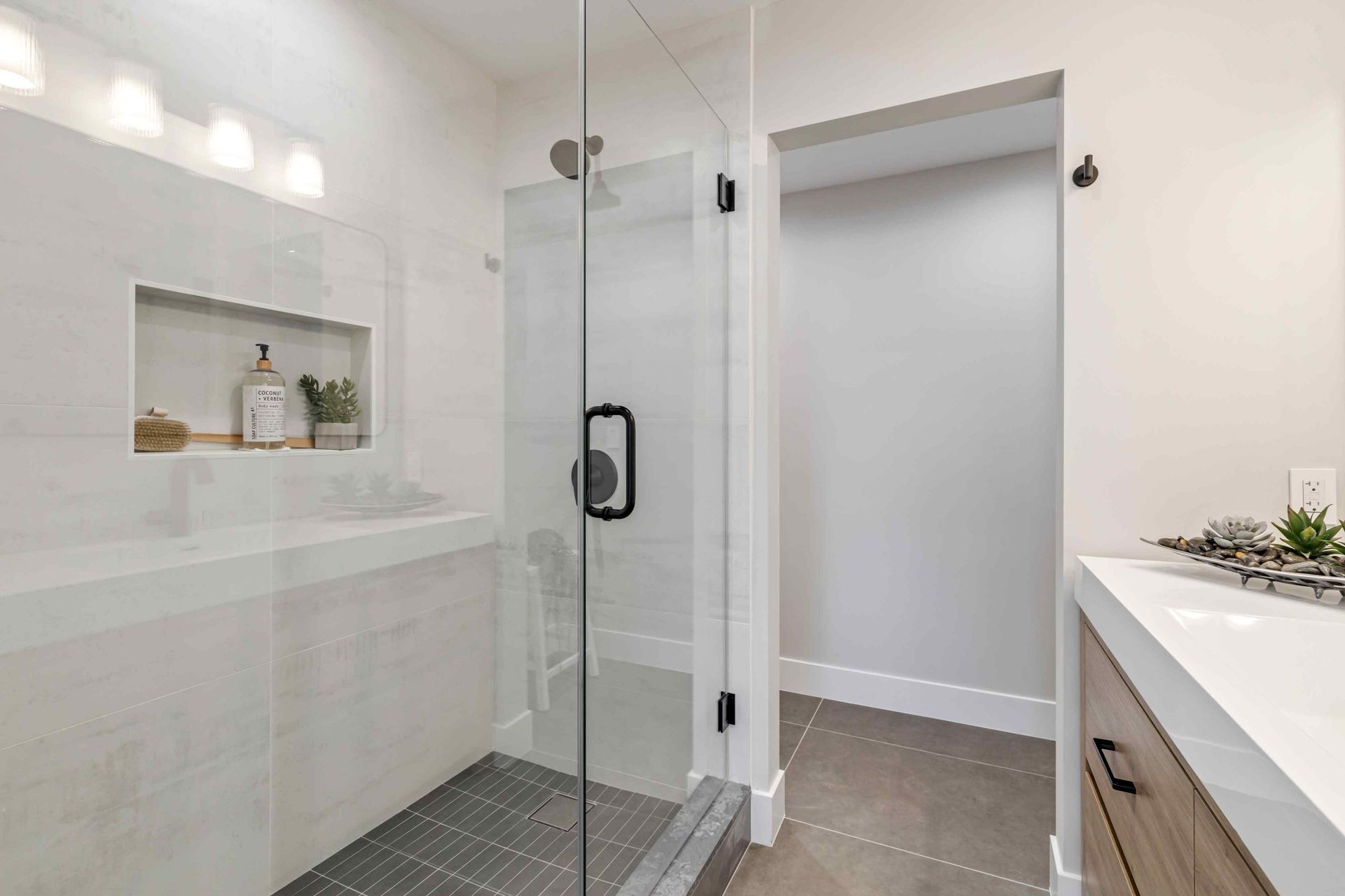 Modern bathroom with glass shower, white countertop, and wooden vanity.