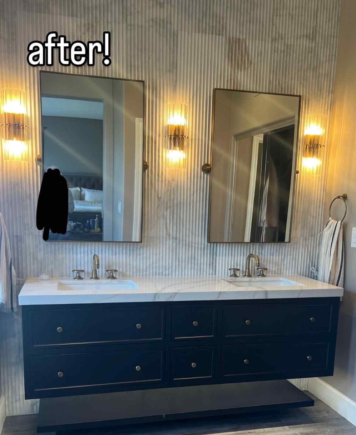 Modern bathroom with dark blue floating vanity, mirrors, and wall sconces.