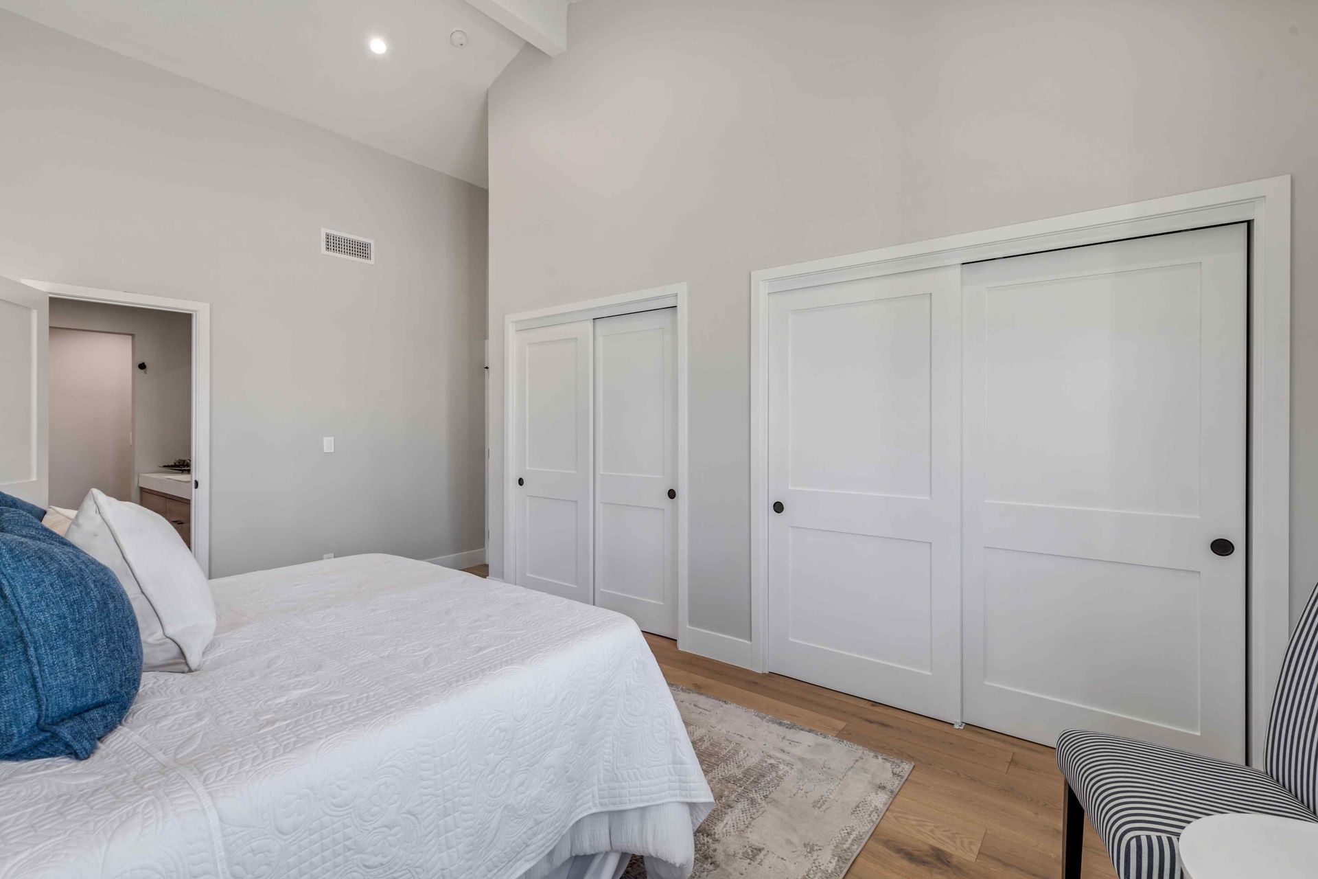 Bedroom with white doors, bed, and a chair with a patterned seat.