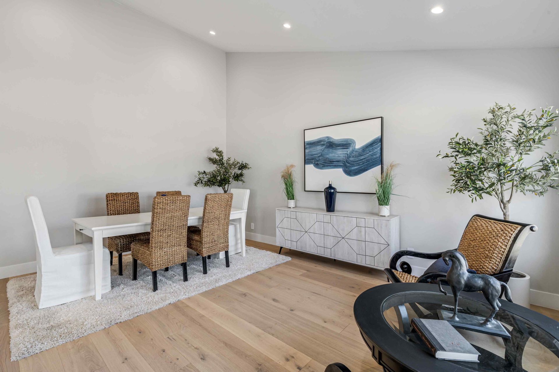 Dining room: White table, patterned chairs, rug, artwork, white credenza, armchair, potted tree.