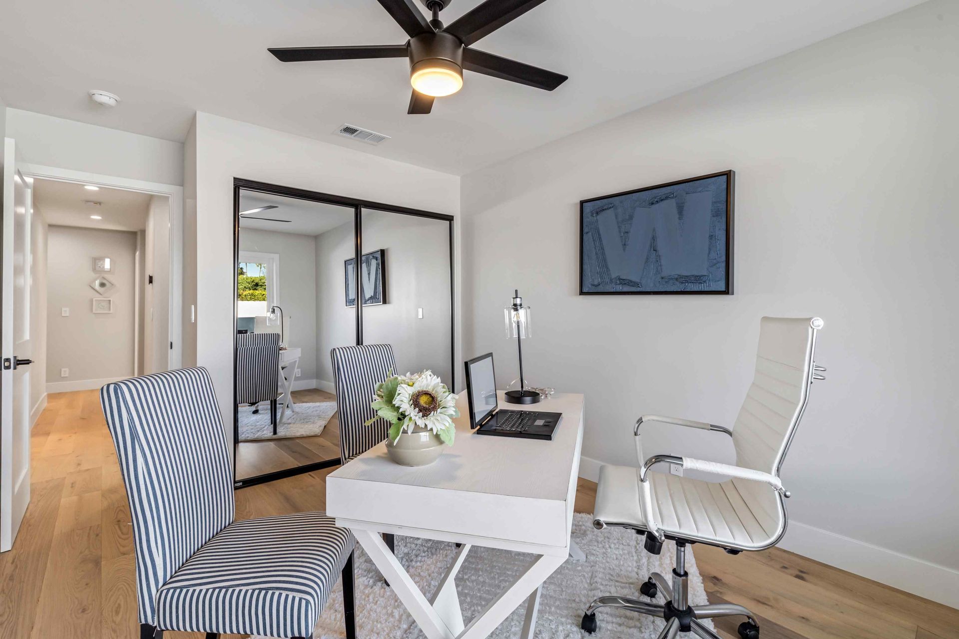 Home office with white desk, office chairs, mirrored closet, and framed art.