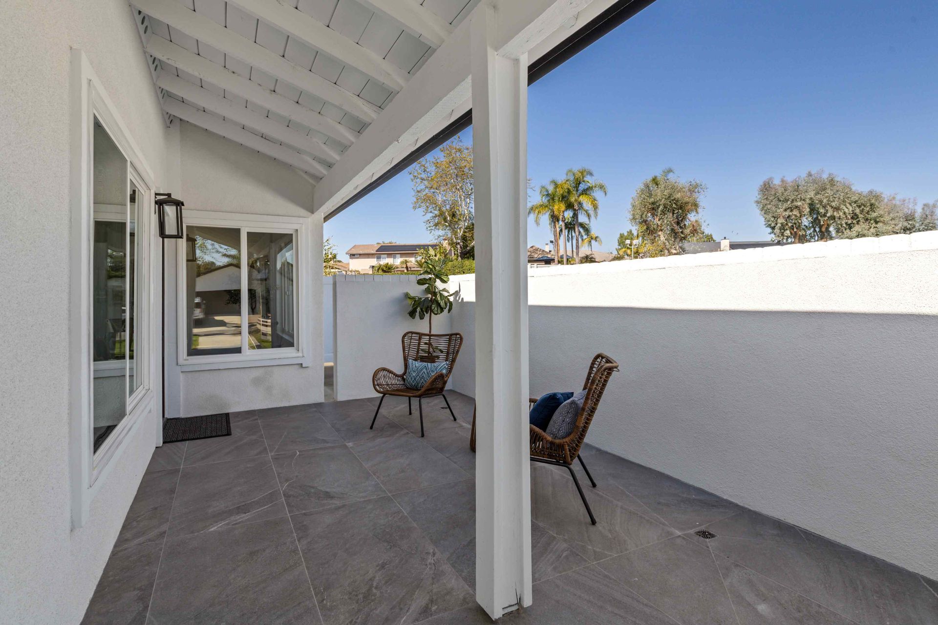 Covered patio with stone flooring, white walls, and two wicker chairs.