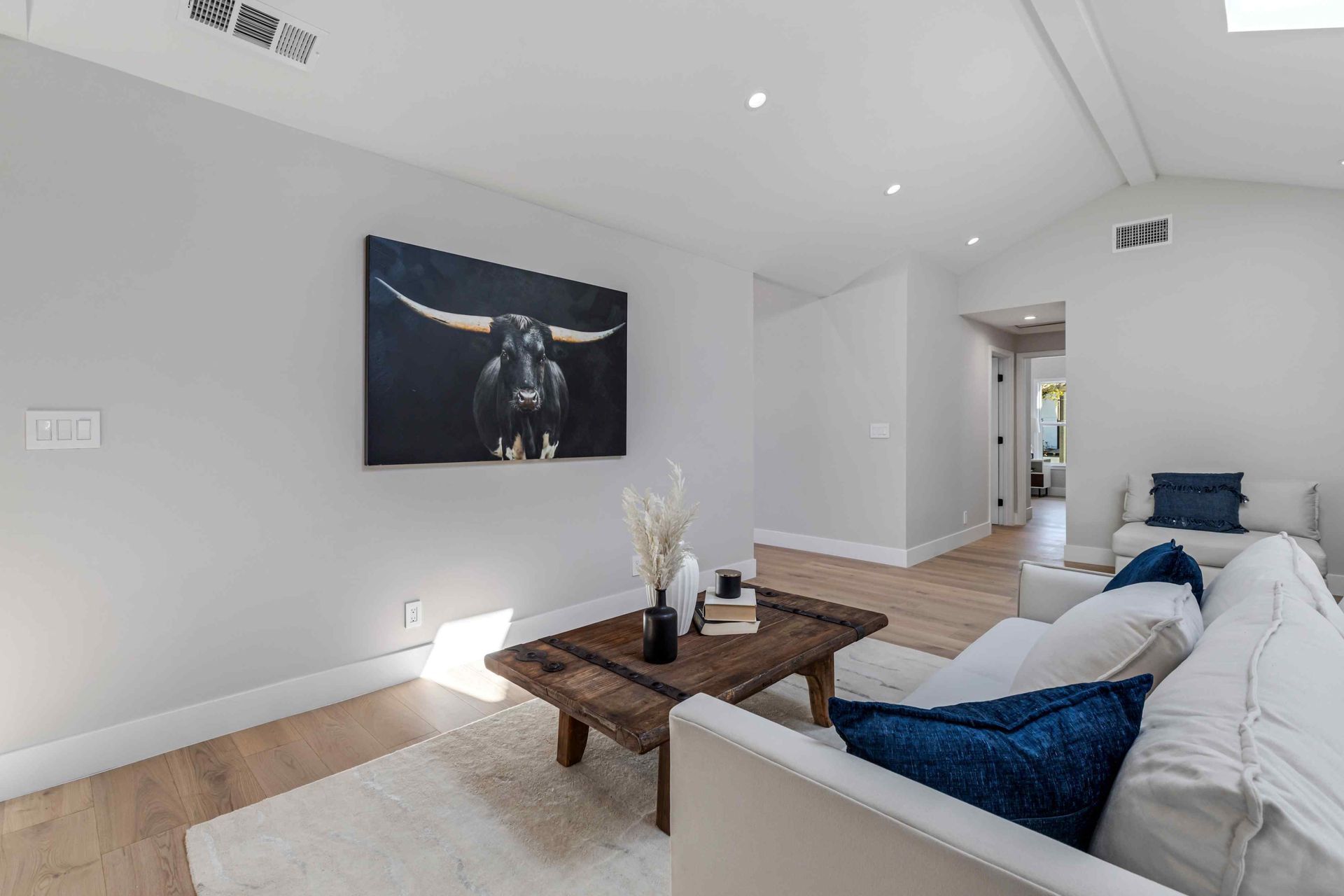 Living room with a black bull painting, white sofas, and wooden coffee table.
