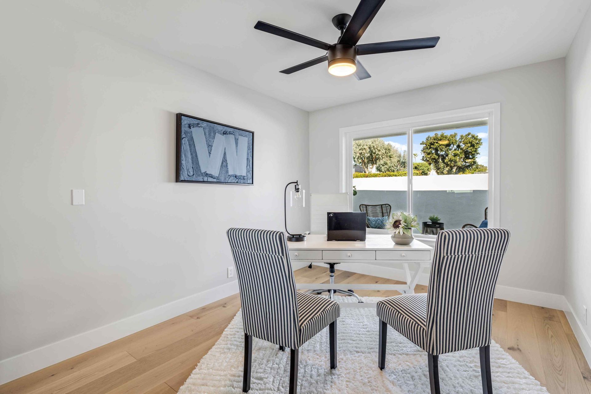 Home office with white desk, zebra-patterned chairs, and sliding glass door, under a dark ceiling fan.