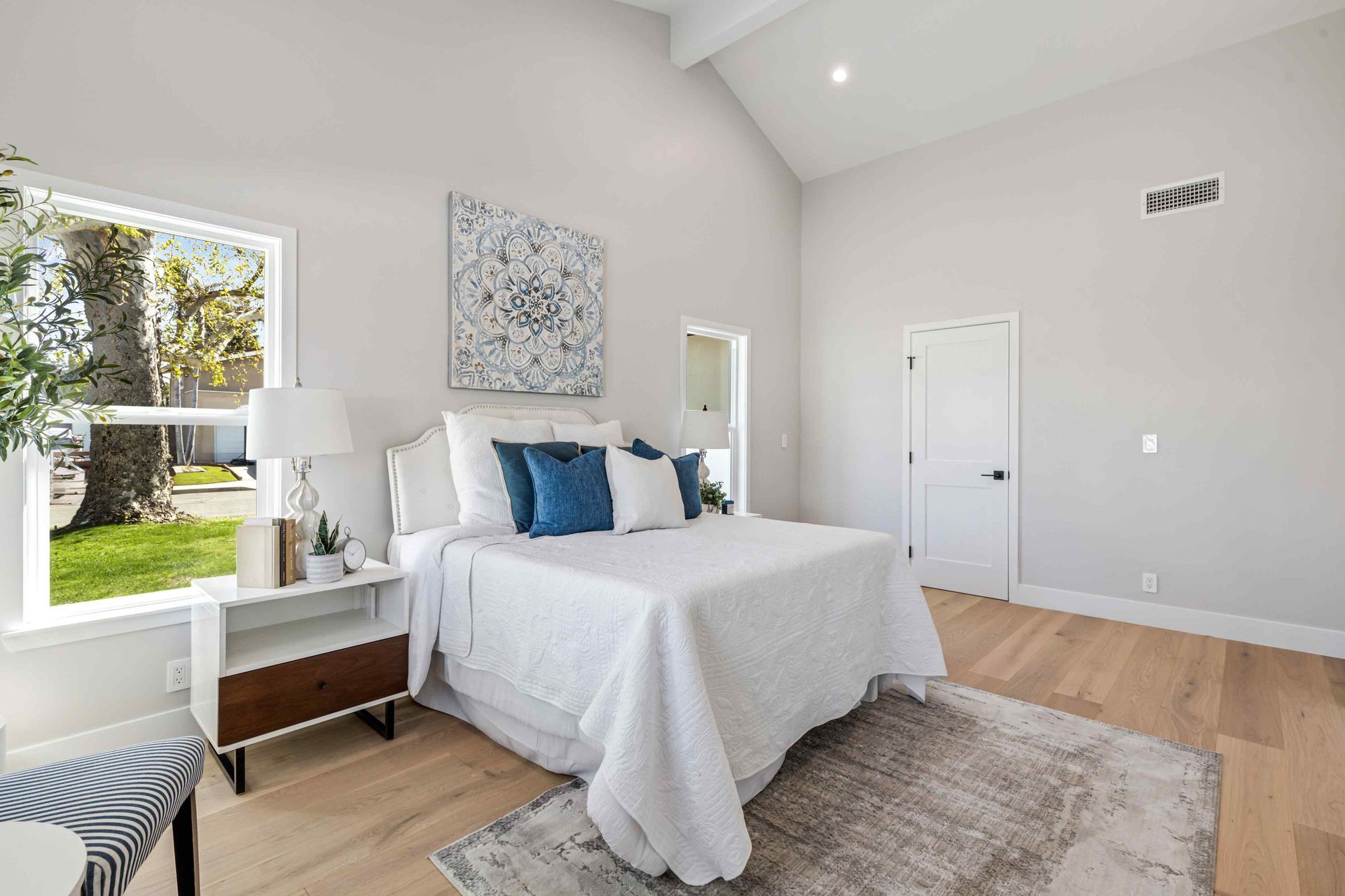 Bedroom with white walls, vaulted ceiling, bed with blue pillows, and wooden floor.