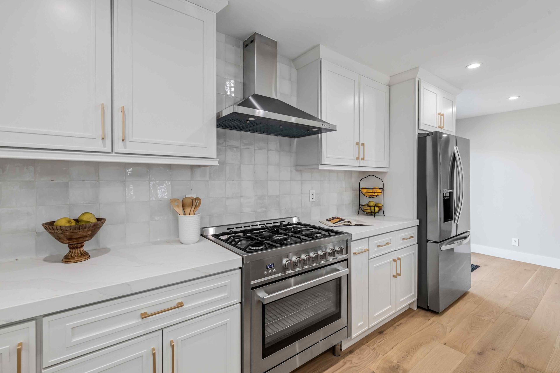White kitchen with stainless steel range, hood, refrigerator.
