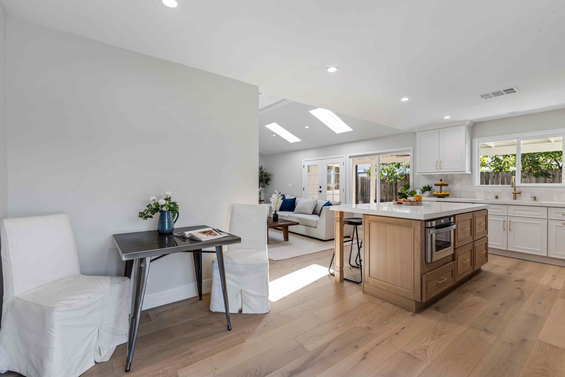 Kitchen with wooden island, white cabinets, and a table with chairs in a light-filled space.