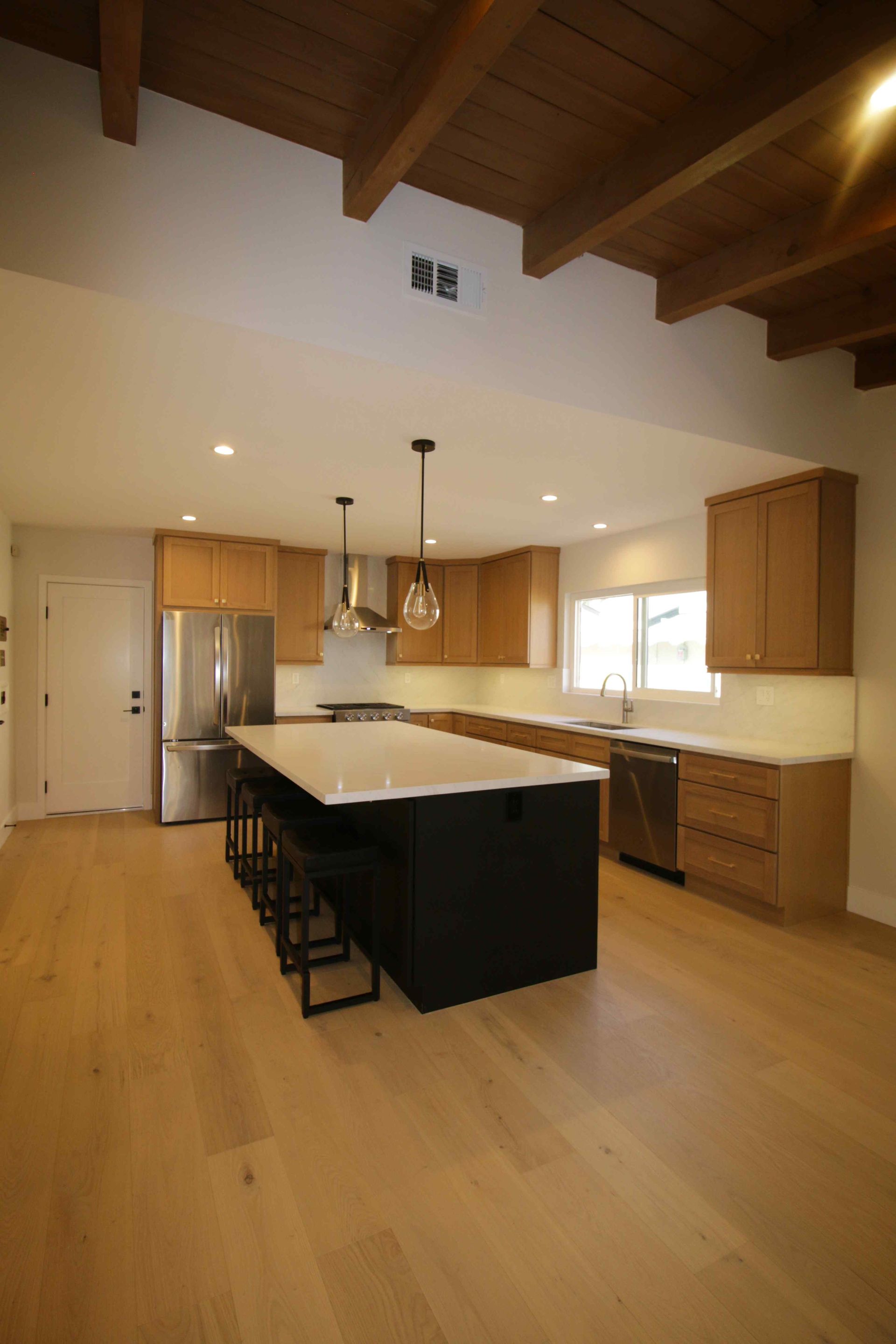 Spacious modern kitchen with a large island, wood floors, and exposed beam ceiling.