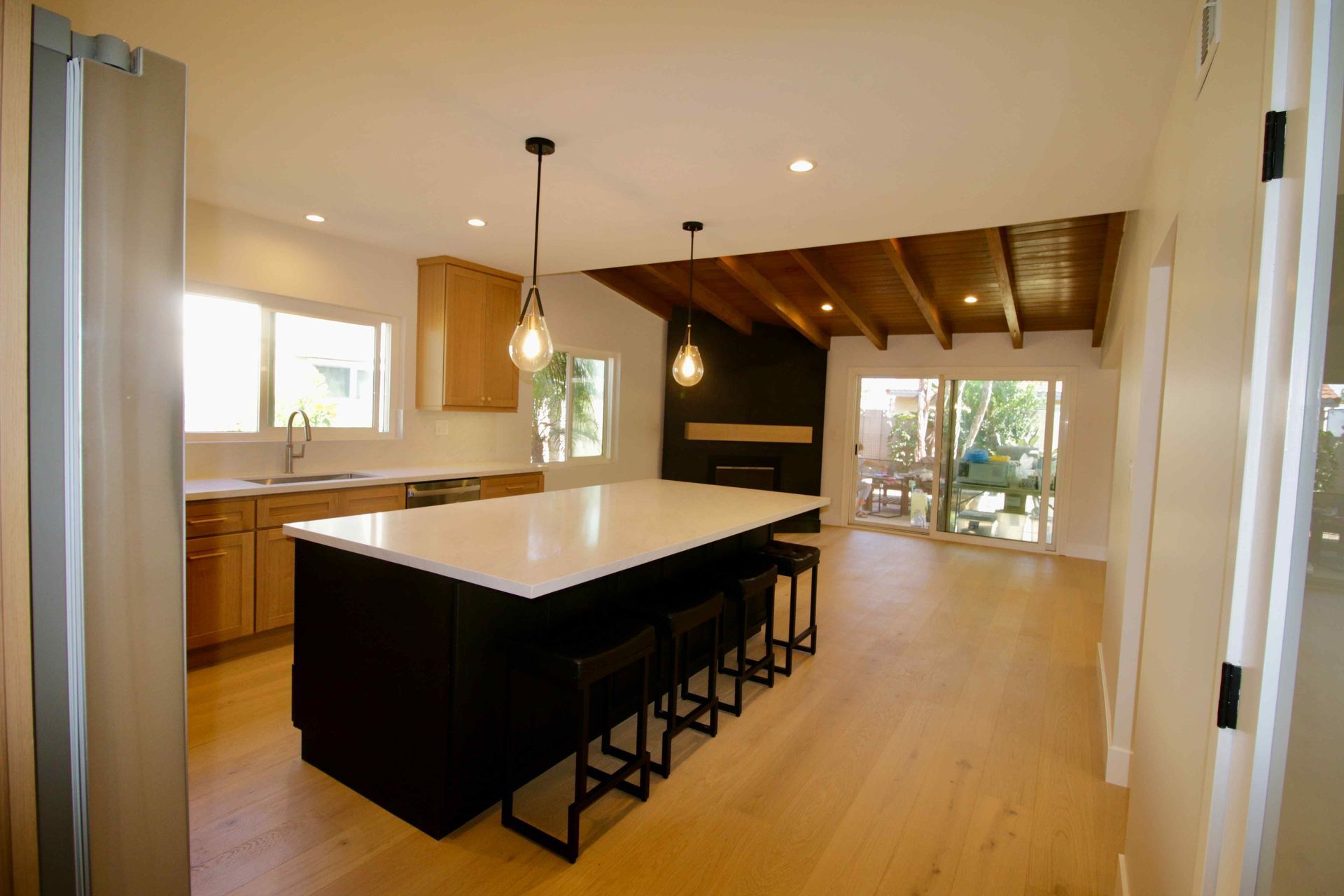 Modern kitchen with a large island, black stools, wood floors, and open view to a patio.