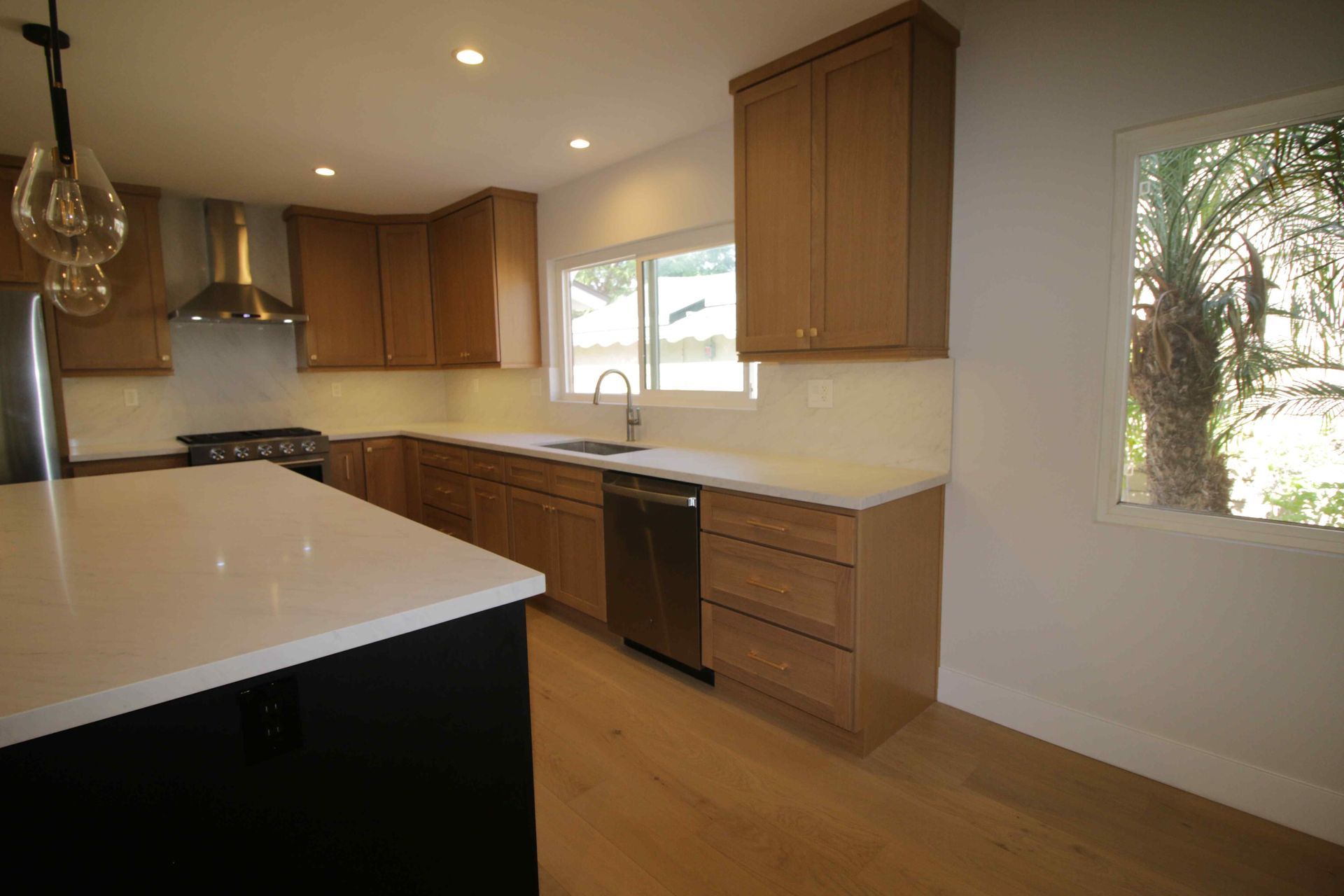 Modern kitchen with wood cabinets, white countertops, and large windows letting in natural light