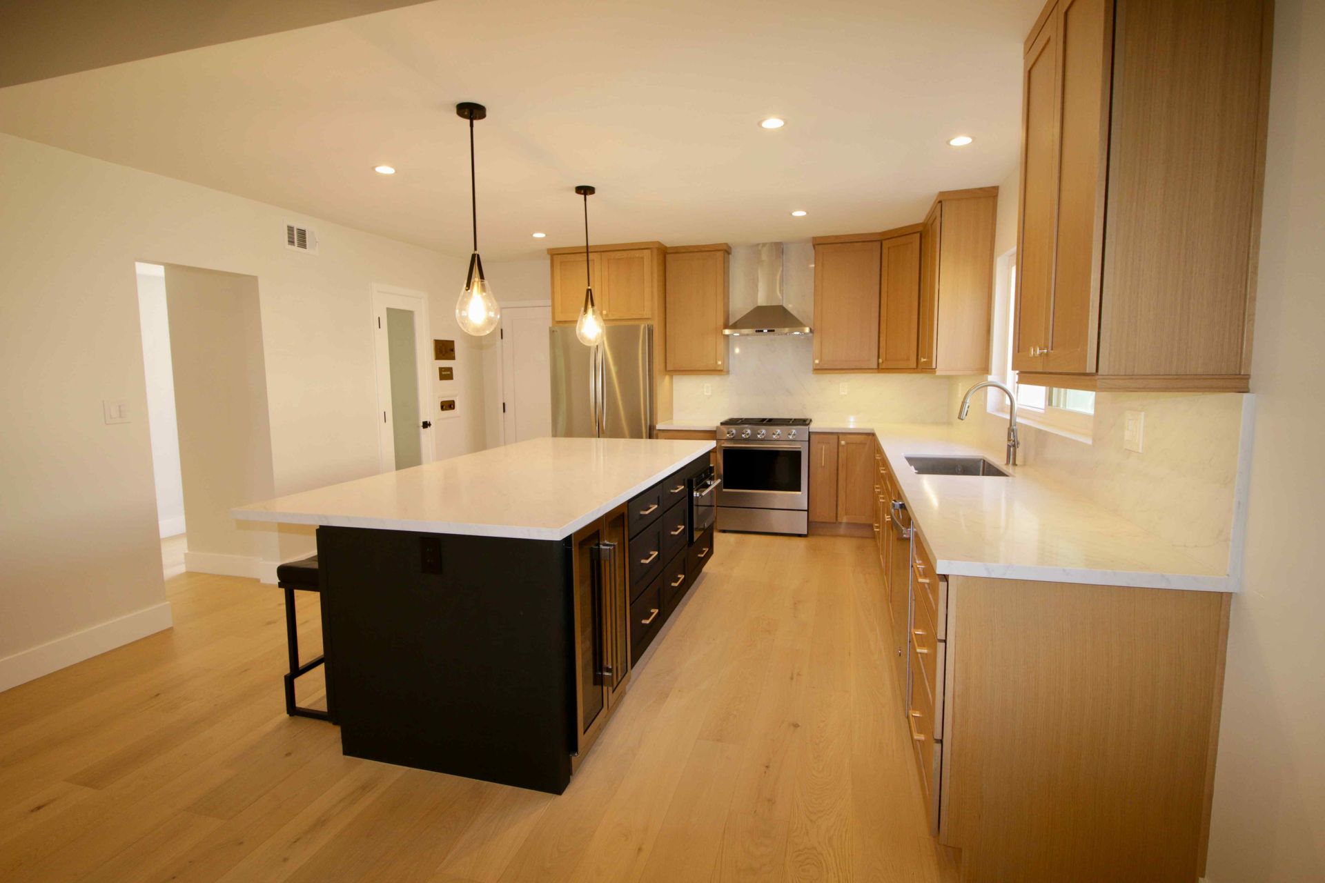 Modern kitchen with a large black island, light wood cabinets, and hardwood floors