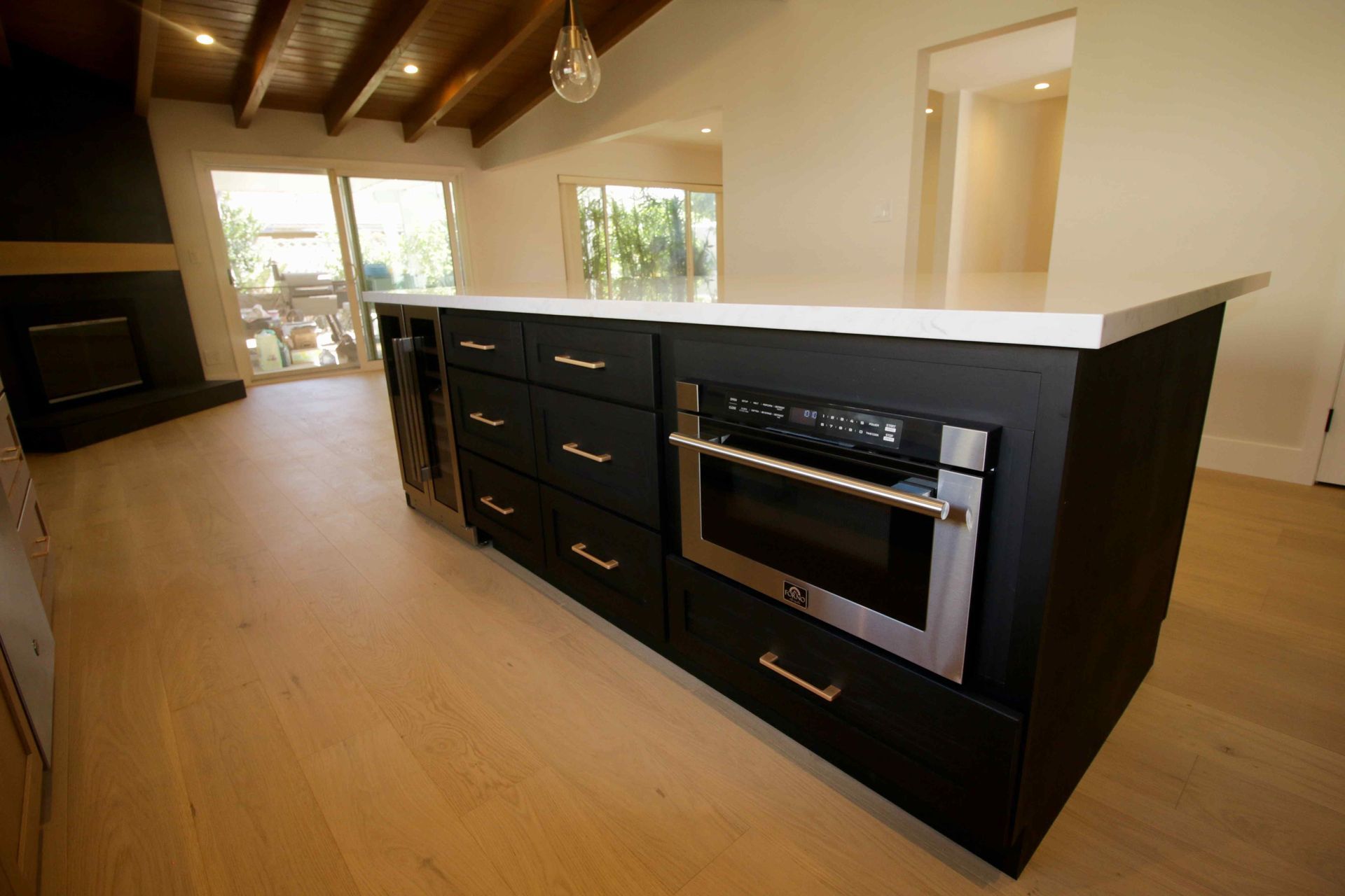Modern kitchen island with black cabinetry, white countertop, and built-in oven in a sunlit room